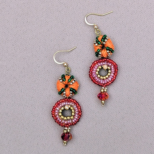 Unique Indian-inspired artisan handmade earrings by Mayaani Jewellery UK, crafted from sustainable, upcycled elements. The design features intricate embroidery with green glass beads, orange hand crochet, solid brass beads and Swarovski-style crystal bicone beads. The circular centrepiece is surrounded by pink and red glass beads creating a vibrant and elegant look. Perfect for eco-conscious fashion lovers, these earrings blend traditional artistry with modern materials.