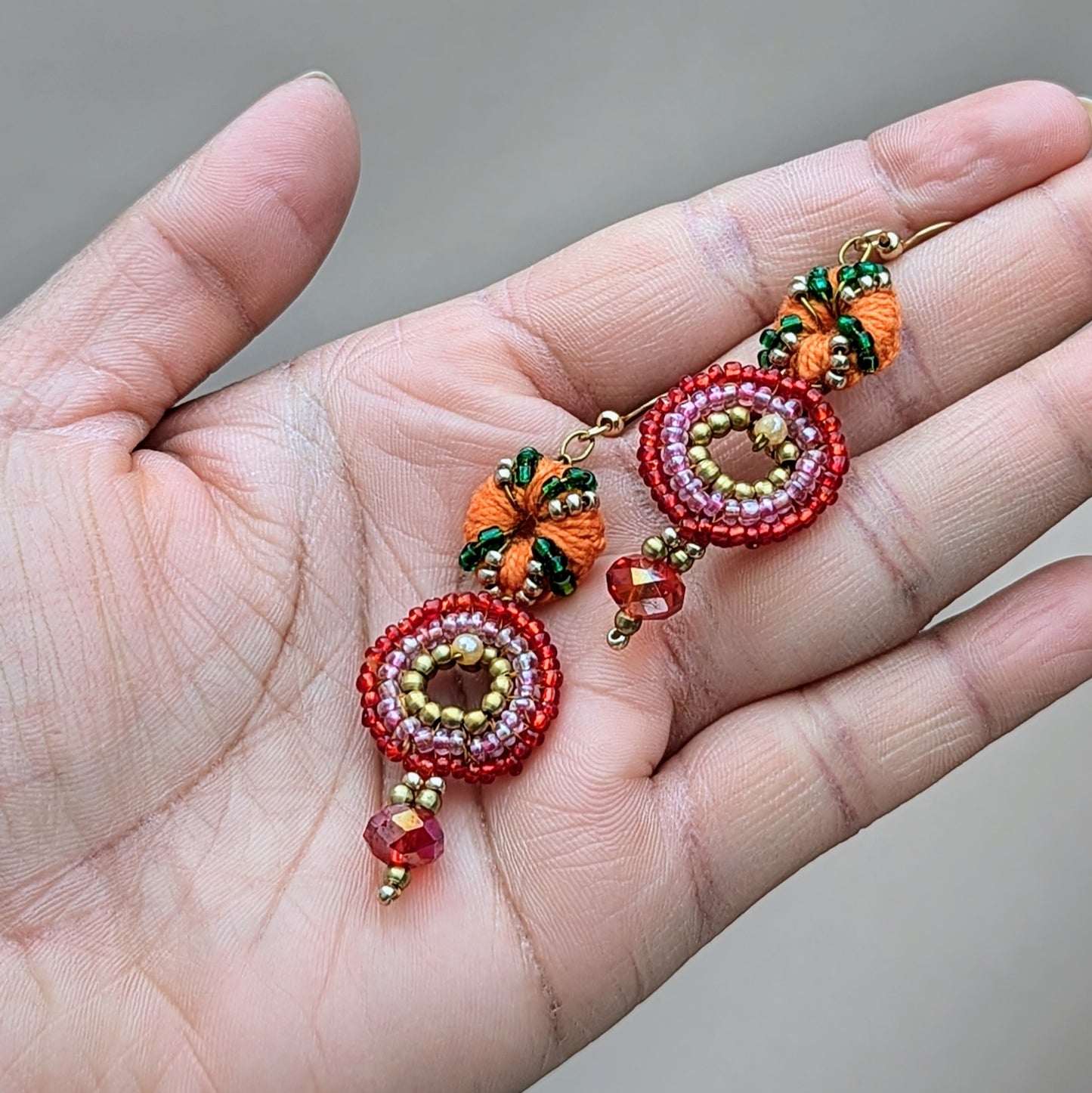 Close-up of Anjali earrings, intricately handcrafted in red, green and gold beadwork with crystal centres and golden accents — a vibrant fusion of Indian tradition and modern artistry.