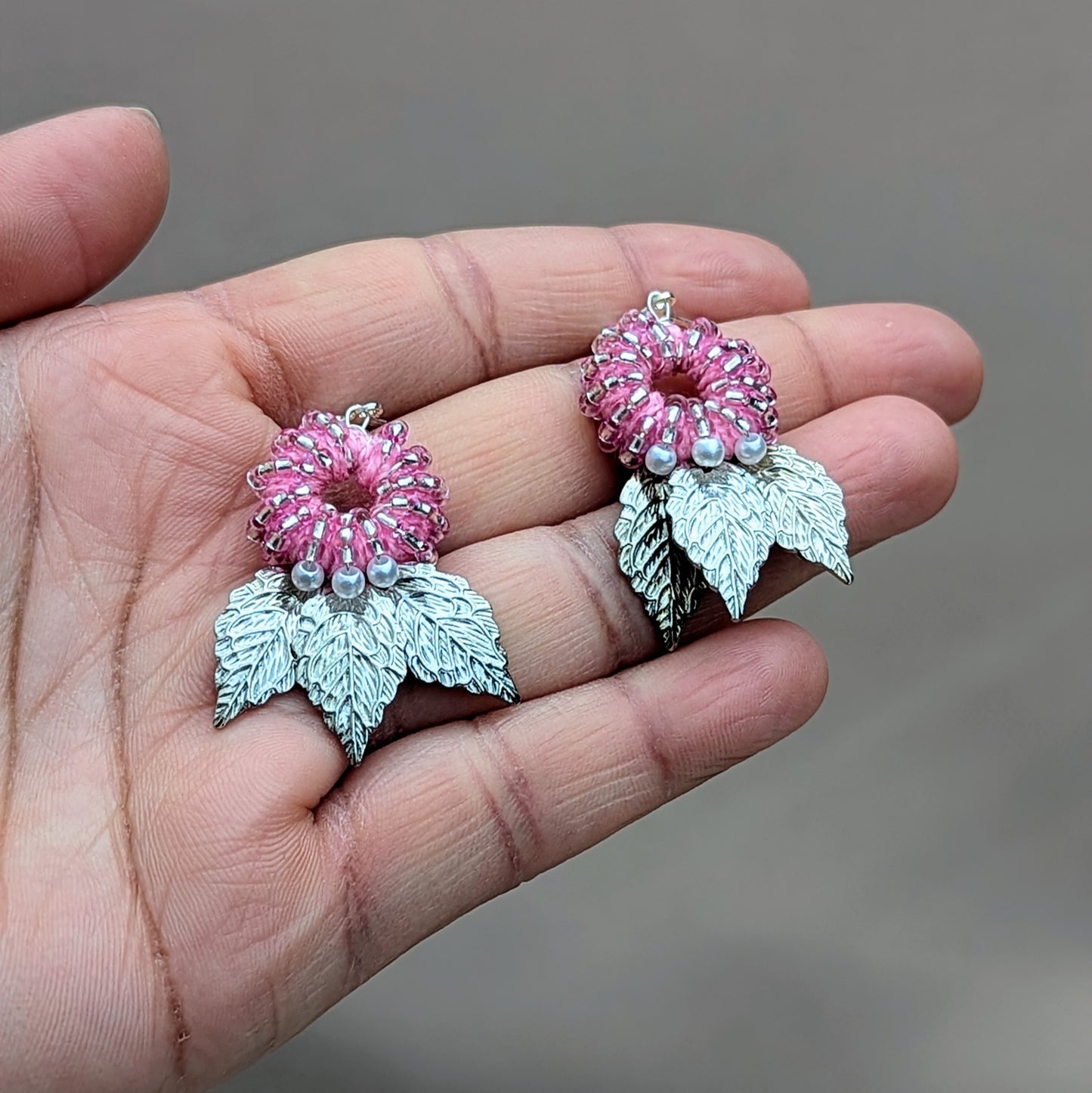 Padmika handmade earrings pictured in the palm of a hand, featuring soft pink beadwork and textured silver leaf drops, sustainable design.
