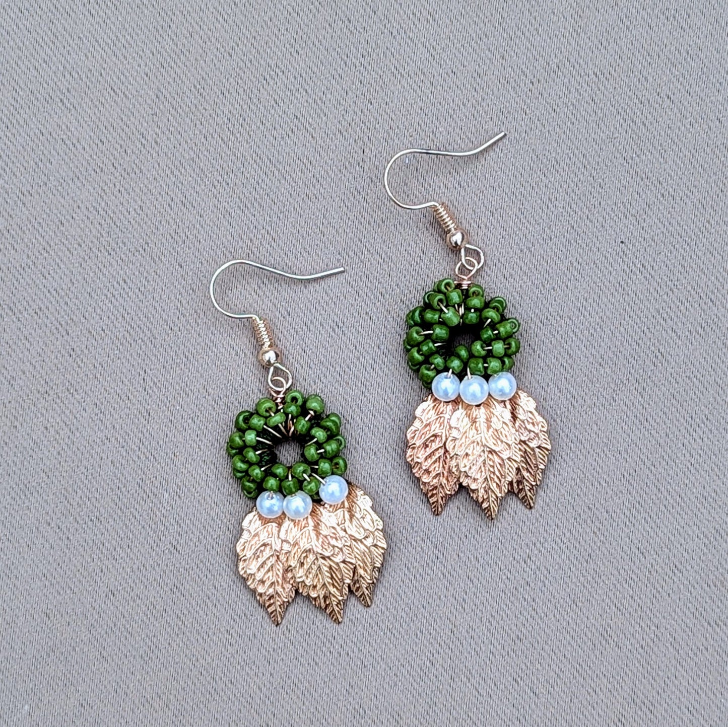 Elegantly handcrafted unique earrings by sustainable UK-based brand Mayaani Jewellery, featuring seed pearl accents with a green circular bead design beneath which dangle three gold leaves. The design reflects artisan craftsmanship with a blend of nature-inspired elements.