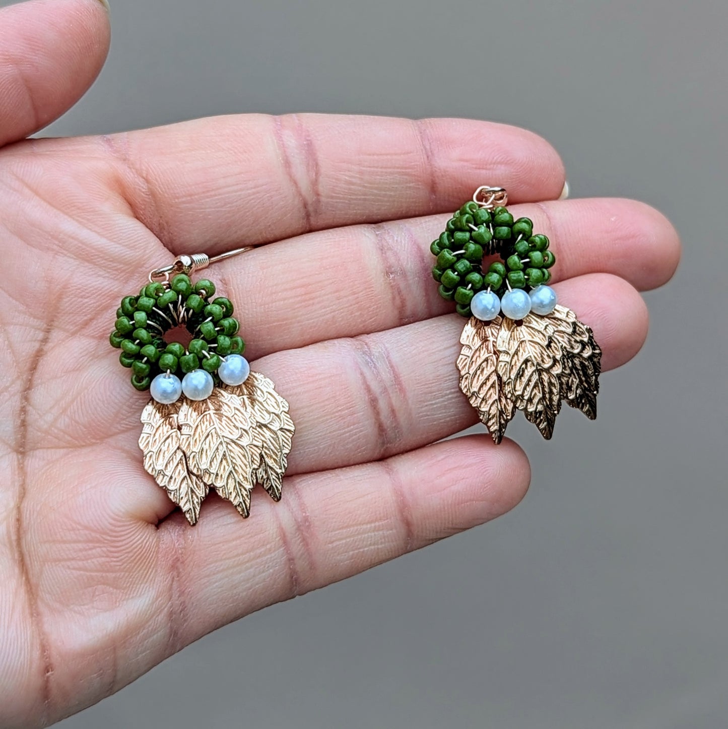 One of a kind earrings handcrafted by Mayaani Jewellery, a sustainable UK brand, featuring a circle of green beads set above intricately detailed gold leaves with seed pearl accents to finish the design. These earrings combine delicate artistry with modern style for a lightweight finish.