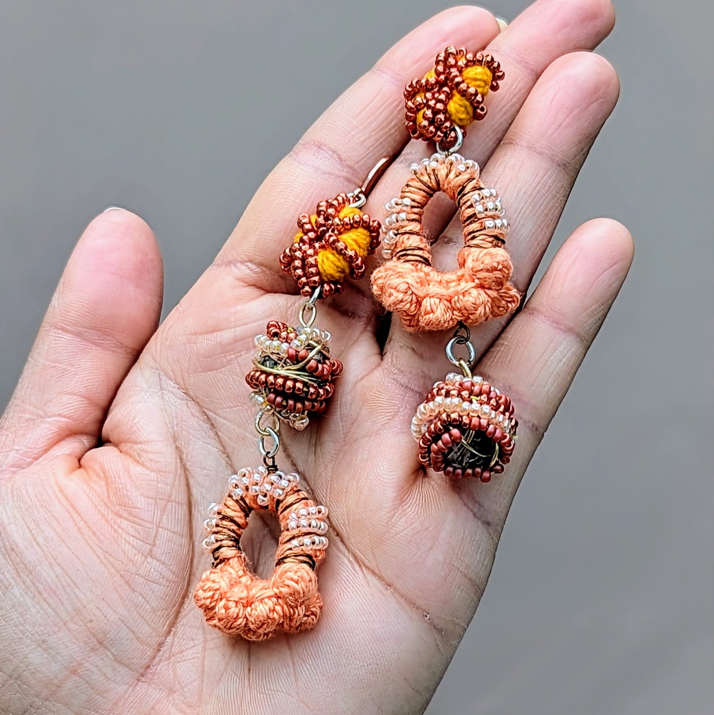 Discover a one-of-a-kind pair of Indian-style earrings in peach, orange, bronze, and rose gold, exclusively handcrafted for sustainable UK brand Mayaani Jewellery. These earrings feature signature concept beads created by in-house artisan Megha, using scraps from the jewellery-making process. Celebrating artistry and sustainability, they are ideal for weddings and special occasions, catering to the modern eco-conscious woman. When worn every day, they make a stunning statement in sustainable style.