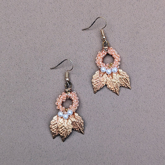 A limited edition pair of Indian Boho-style earrings, artisan handcrafted for Mayaani Jewellery UK. The design features intricately detailed gold-plated leaves, combined with hand-crocheted loops adorned with small peach beads and white seed pearls. The earrings showcase a delicate balance of hand wire work, crochet and beadwork, merging traditional craftsmanship with contemporary elegance. These sustainable earrings are part of a collection from a UK-based brand focussing on eco-conscious fashion.