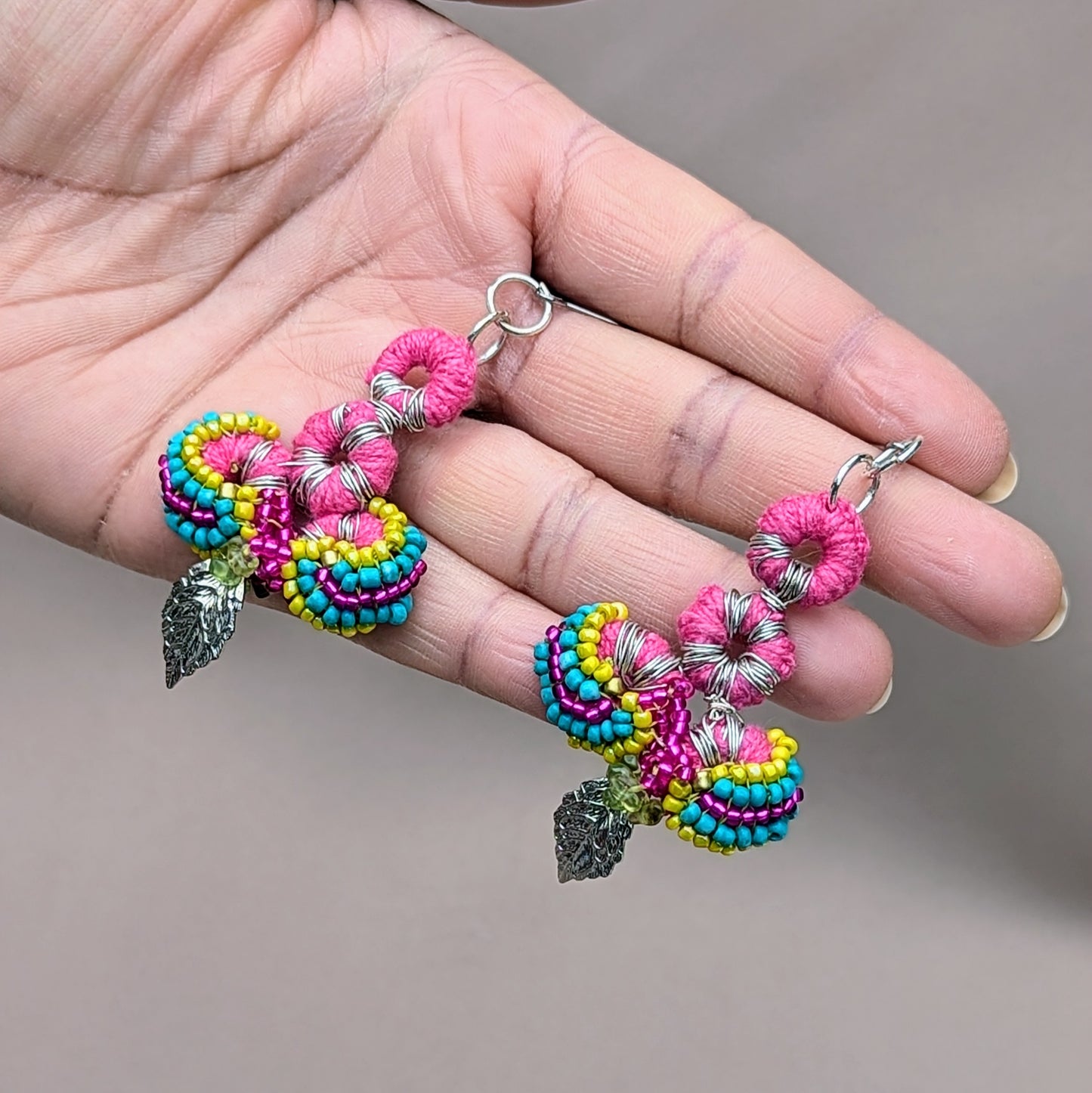 These artisan earrings, crafted by Mayaani Jewellery, a UK-based sustainable brand, feature Indian-inspired designs with crochet in vibrant pink, multi-coloured beadwork, and silver leaf charms. Made from upcycled materials, including peridot gemstone chips, they are lightweight and comfortable. A reflection of Mayaani's eco-friendly approach, these earrings combine bold colours with thoughtful, sustainable craftsmanship.