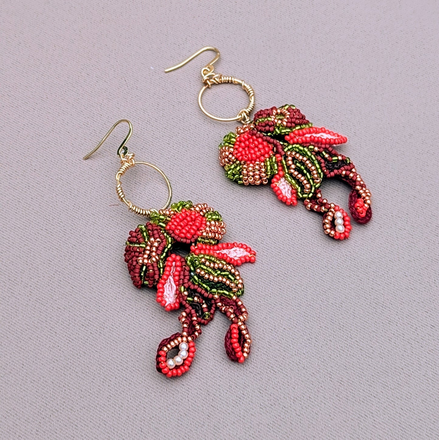 A pair of expertly handcrafted earrings, designed exclusively for Mayaani Jewellery, a sustainable UK brand. These earrings feature intricate beadwork in red, green, brown, and gold, with a delicate gold wire wrapped hoops. The Indian-inspired design blends floral aesthetics for comfortable wedding and occasion wear with an artistic approach to jewellery.