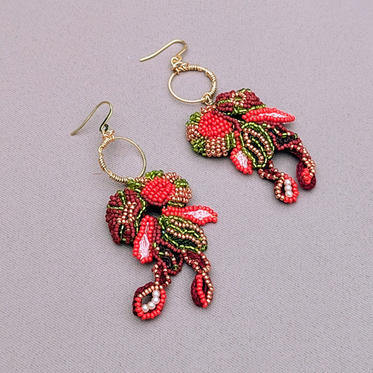 A pair of expertly handcrafted earrings, designed exclusively for Mayaani Jewellery, a sustainable UK brand. These earrings feature intricate beadwork in red, green, brown, and gold, with a delicate gold wire wrapped hoops. The Indian-inspired design blends floral aesthetics for comfortable wedding and occasion wear with an artistic approach to jewellery.