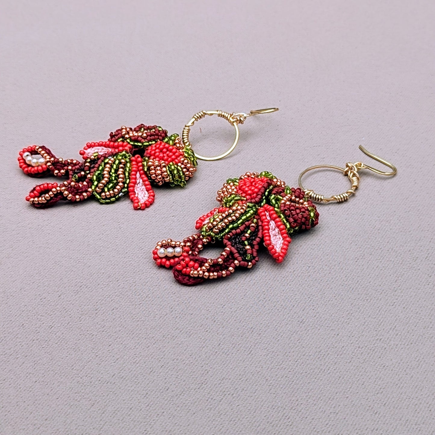 A side view of a unique pair of earrings exclusively crafted for sustainable UK brand Mayaani Jewellery showcasing vibrant beadwork in red, green, gold and brown. The comfortable Indian-inspired design is hung from a wire wrapped gold hoop for style with an artistic edge.