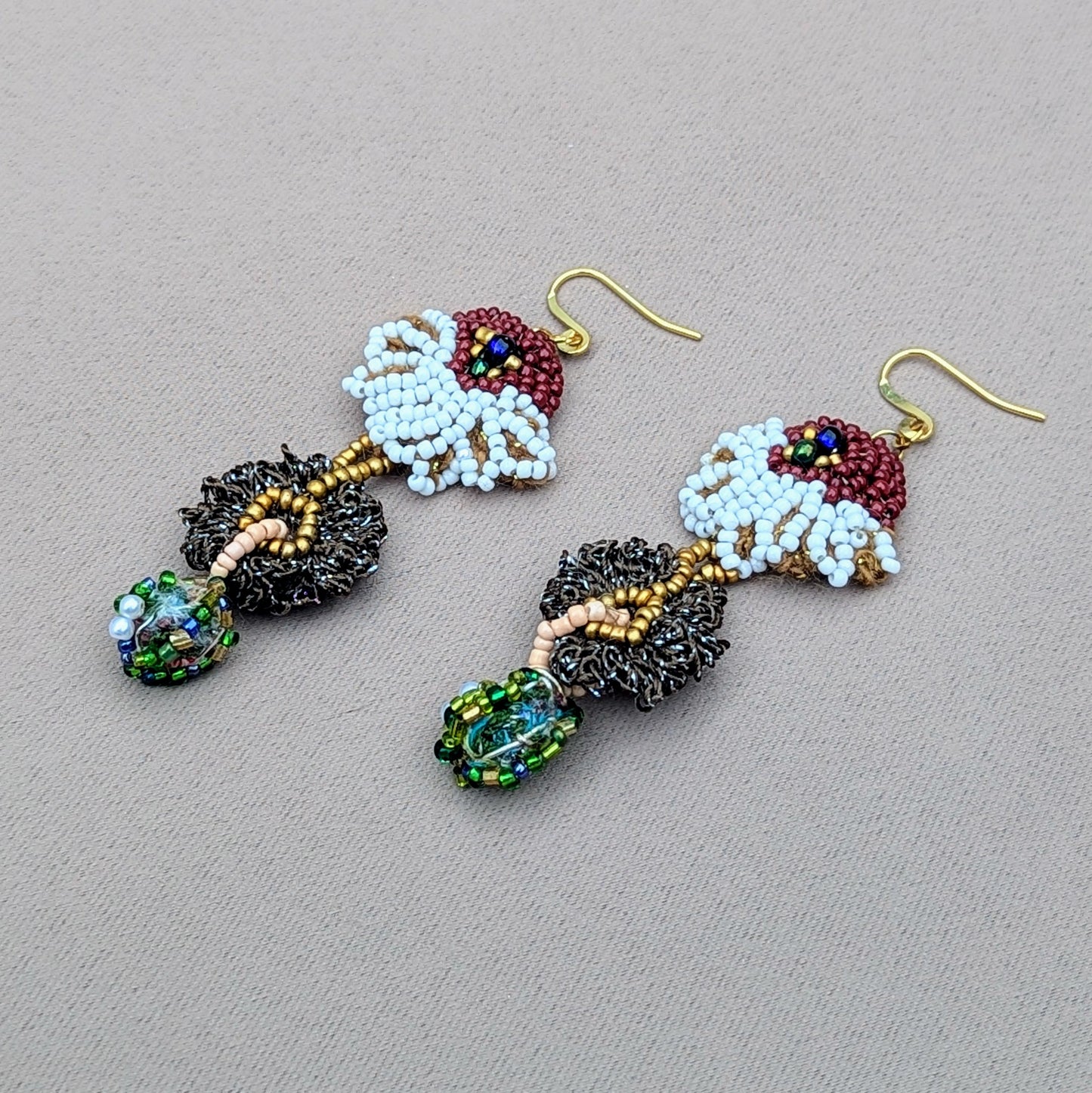 SweetEllaBella earrings resting gently on hand, showcasing intricate floral beadwork in rich greens and golds — a radiant symbol of renewal and sustainable artistry.