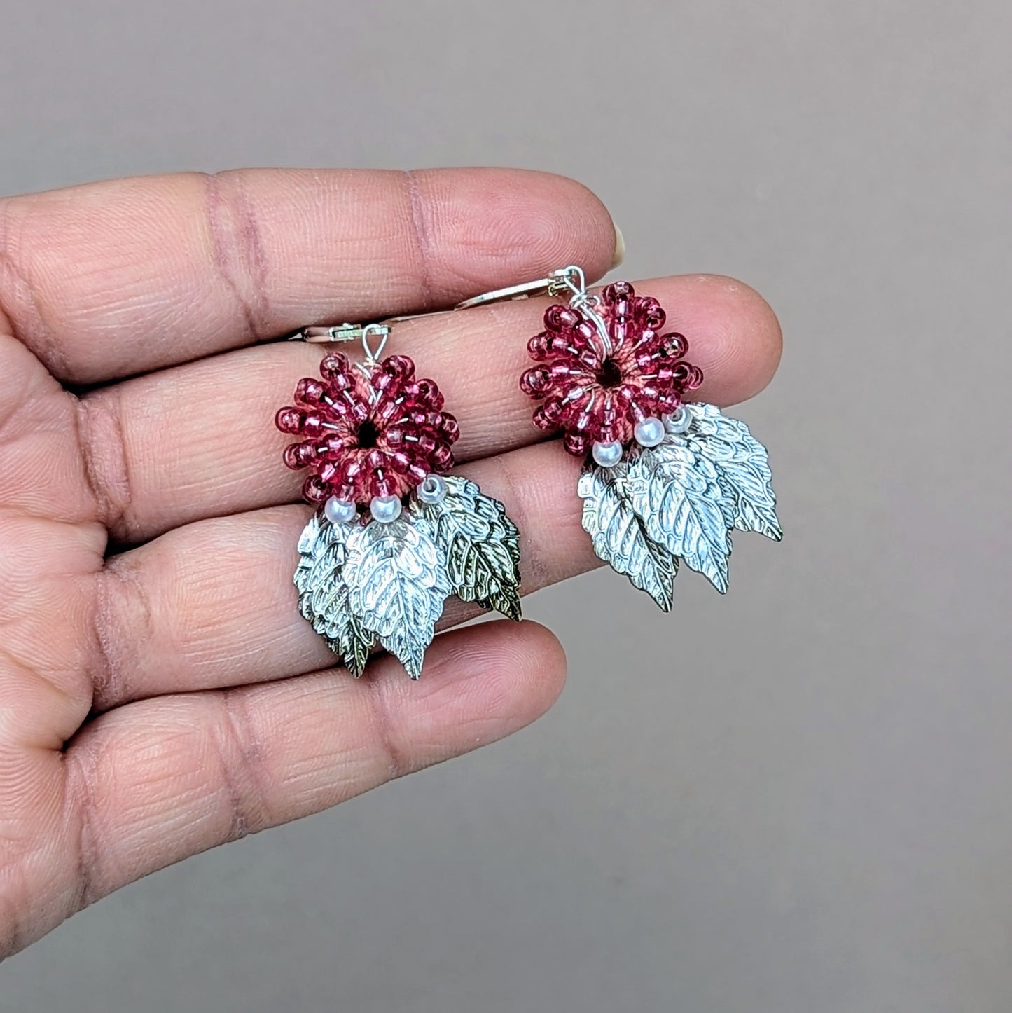 Presenting a limited edition set of eye-catching watermelon red earrings, available in a unique range of colors exclusive to Mayaani Jewellery, a sustainable UK brand. These earrings showcase a pink hand-crocheted base beautifully embellished with hand-wrapped watermelon red and ivory pearl seed beads. Detailed silver-plated leaf charms and secure 925 stamped sterling silver clasps complete the design, making them a playful yet elegant accessory for any occasion.