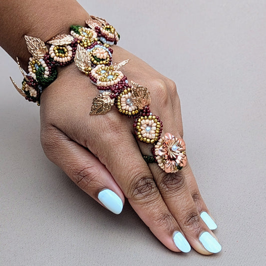 A hand modelling Mayaani 5-in-1 Indian hand bracelet / haath phool in a modern reimagination of classic bridal red, green and gold colours. Pictured against a neutral soft grey backdrop.