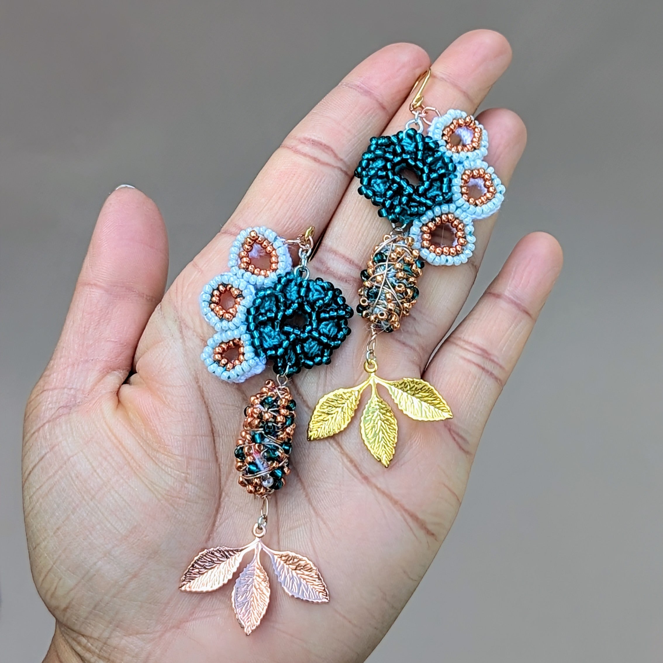 Hand holding a one-of-a-kind pair of asymmetric blue and gold Indian style scrap bead earrings handcrafted in an innovative Mayaani Jewellery concept developed to reduce waste.