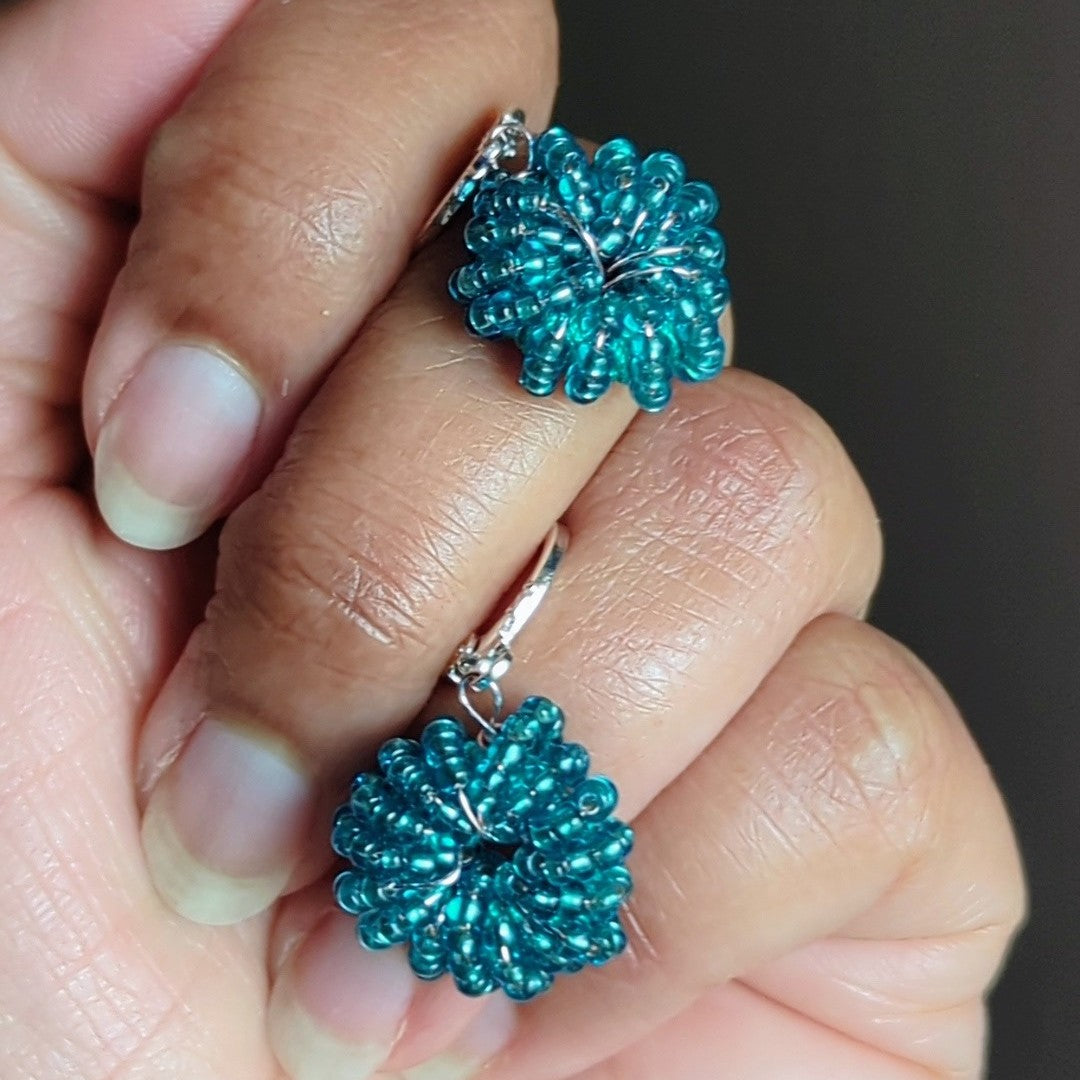Hand holding one-of-a-kind blue handmade earrings crafted with silver-lined seed beads and rose gold copper wire by Mayaani Jewellery UK.