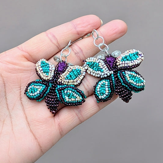 Hand holding an artisan made pair of purple, blue, cream and silver Mayaani Jewellery butterfly earrings in celebration of transformation and renewal.