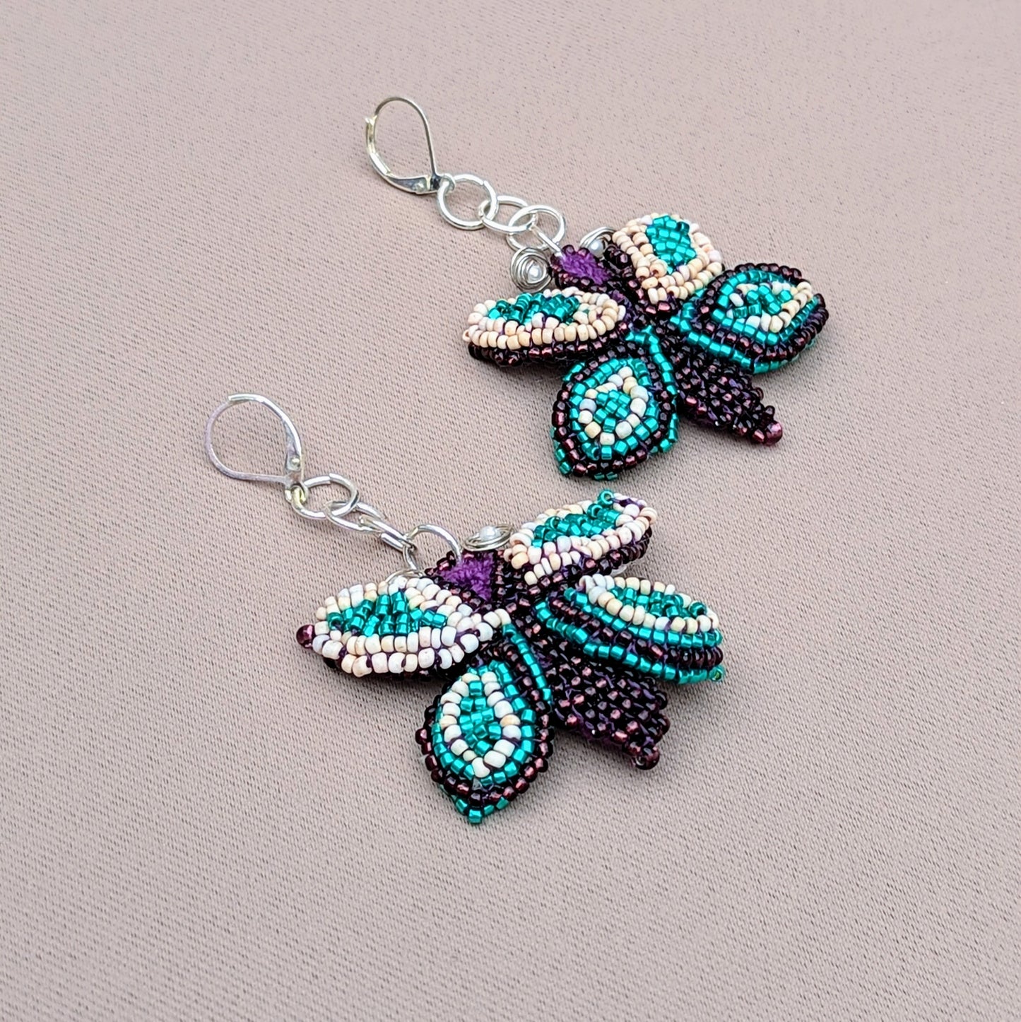 A flat lay view of a butterfly pair of sustainably handcrafted earrings exclusive to Mayaani Jewellery UK featuring blue, purple, cream and silver.