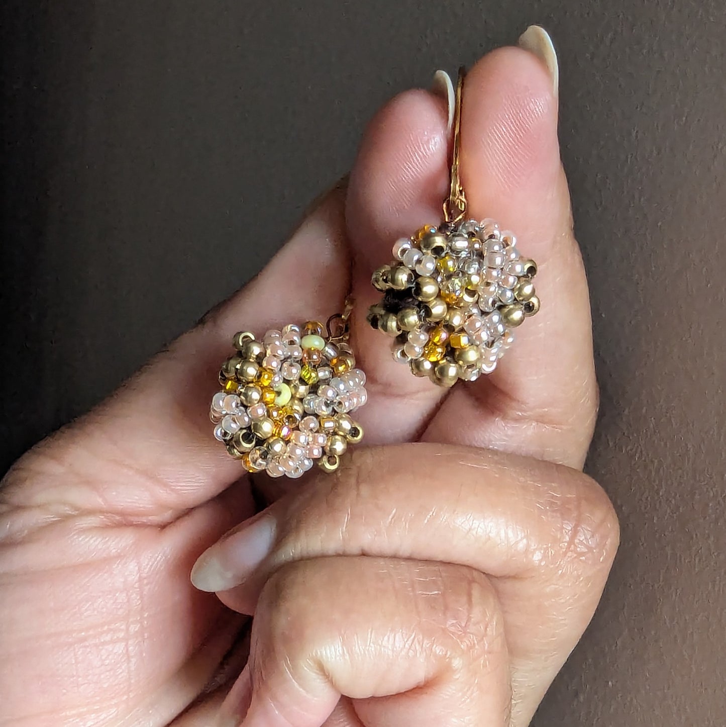 Hand holding golden handmade beaded earrings crafted by Mayaani Jewellery UK.