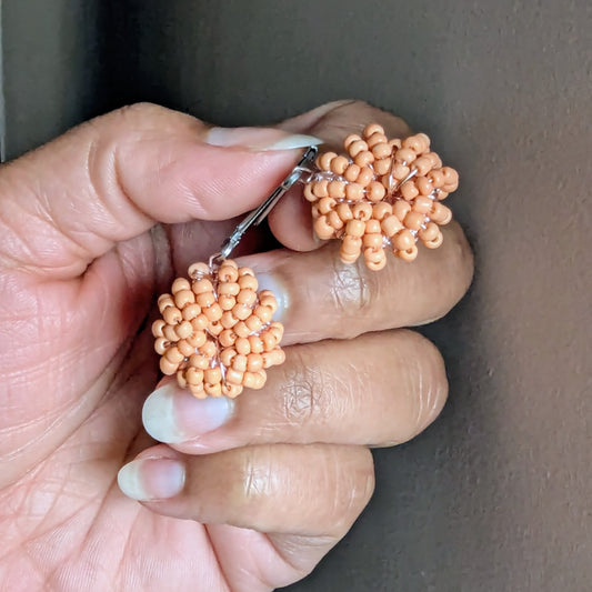 Close-up of artisan-made peach seed bead earrings with gold-plated clasps.