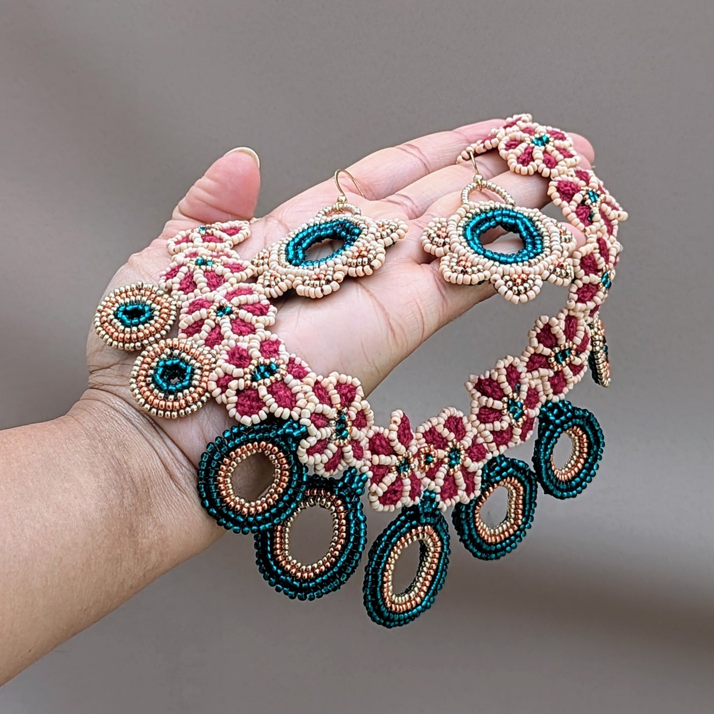One of a kind Indian bridal necklace and earring set, held on the palm of a hand, in emerald green, red, peach, gold and rose gold handcrafted in the UK for sustainable brand Mayaani Jewellery.
