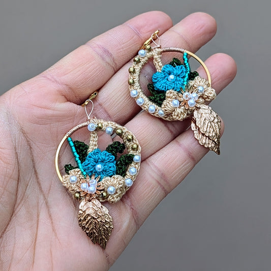 Hand presenting a home studio made one of a kind designer pair of Indian heritage inspired earrings in blue and gold with pearl seed bead  & solid brass bead accents, exclusive to sustainable UK brand Mayaani Jewellery.