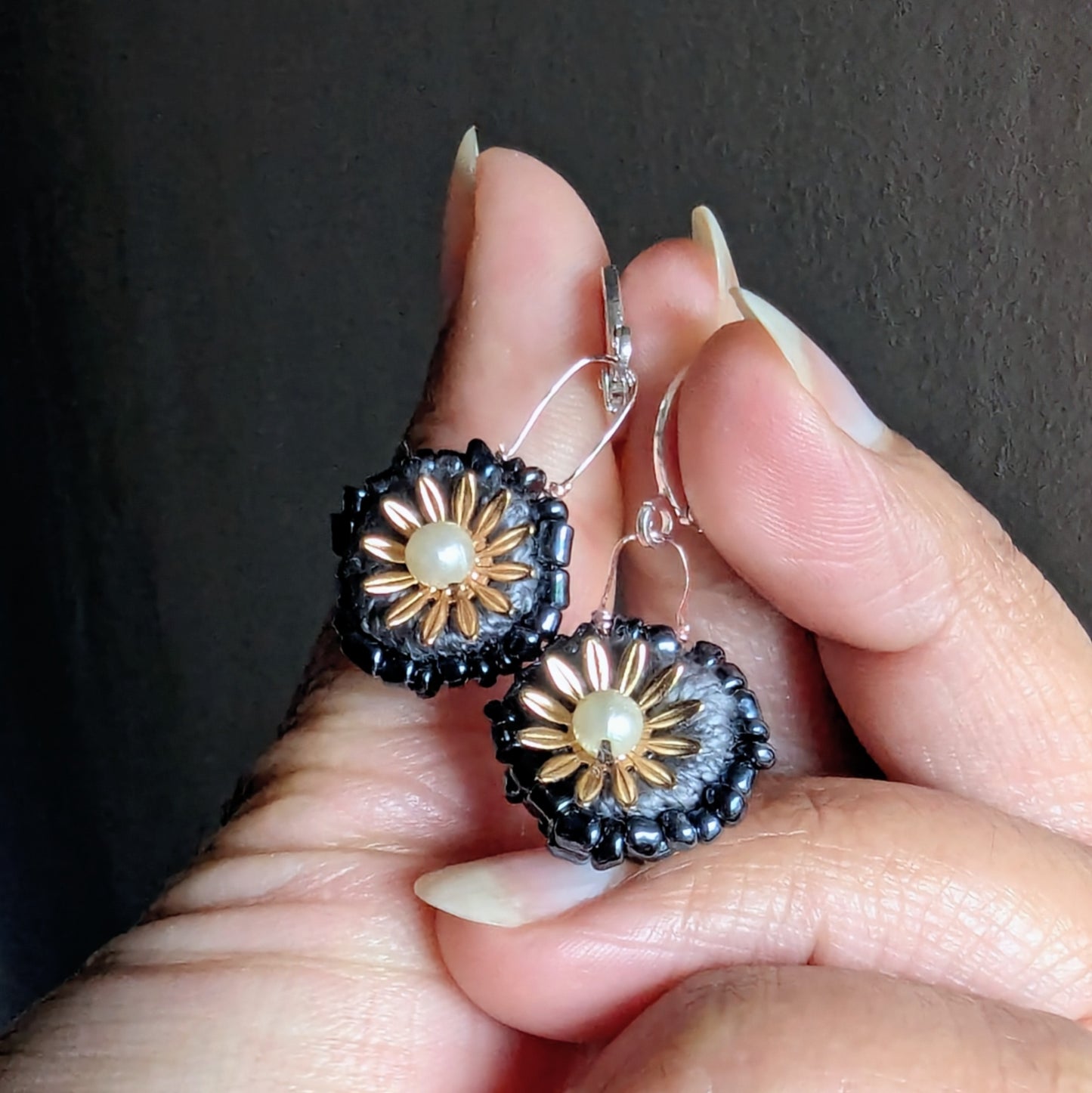 Close up of fingers holding a sustainably crafted grey gold floral inspired earrings with a pearl centre.
