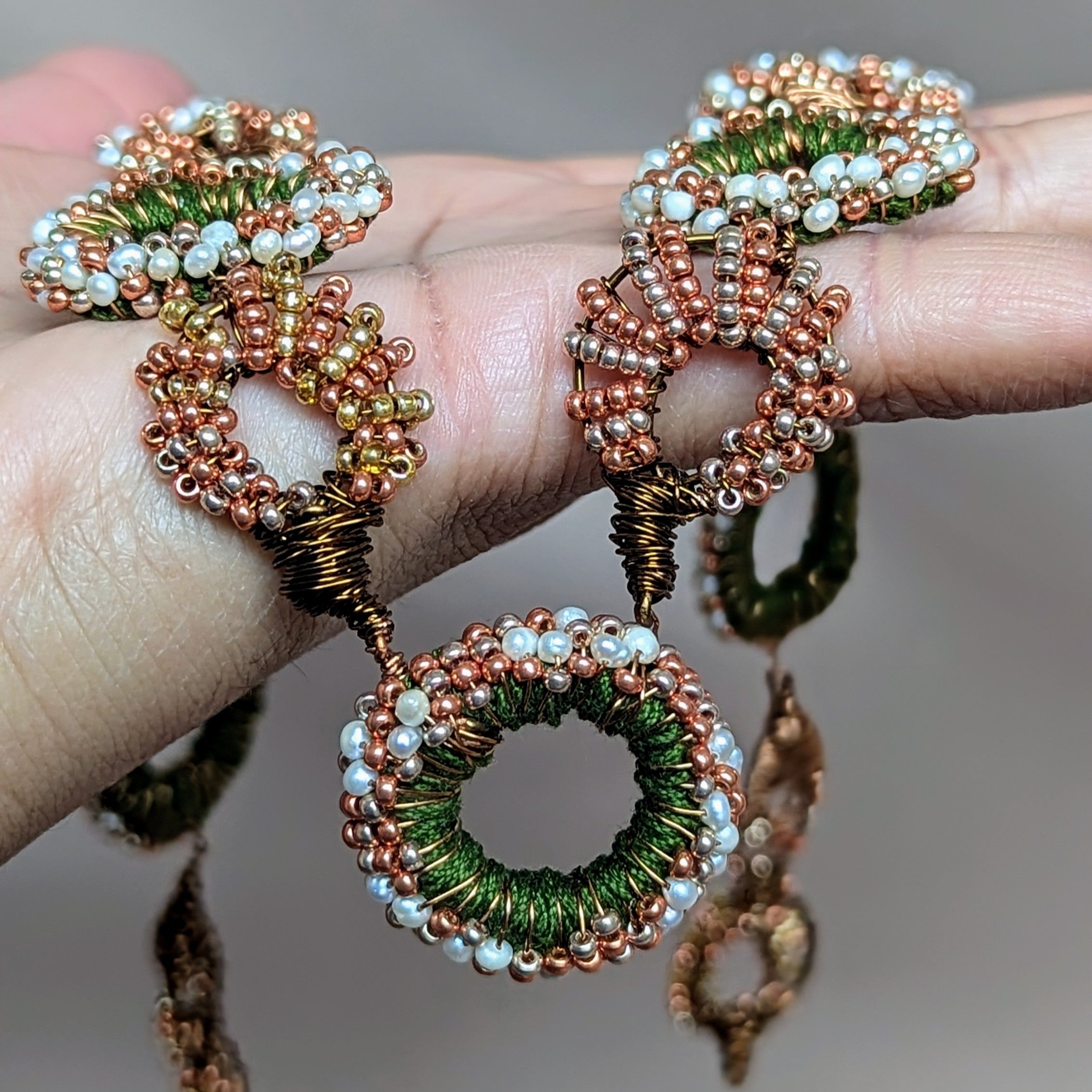 Close up of an artisan handcrafted green, bronze, gold, copper and freshwater pearl statement Indian heritage inspired necklace handcrafted at Mayaani Jewellery UK featuring hand crochet, beadwork and wire wrapping.