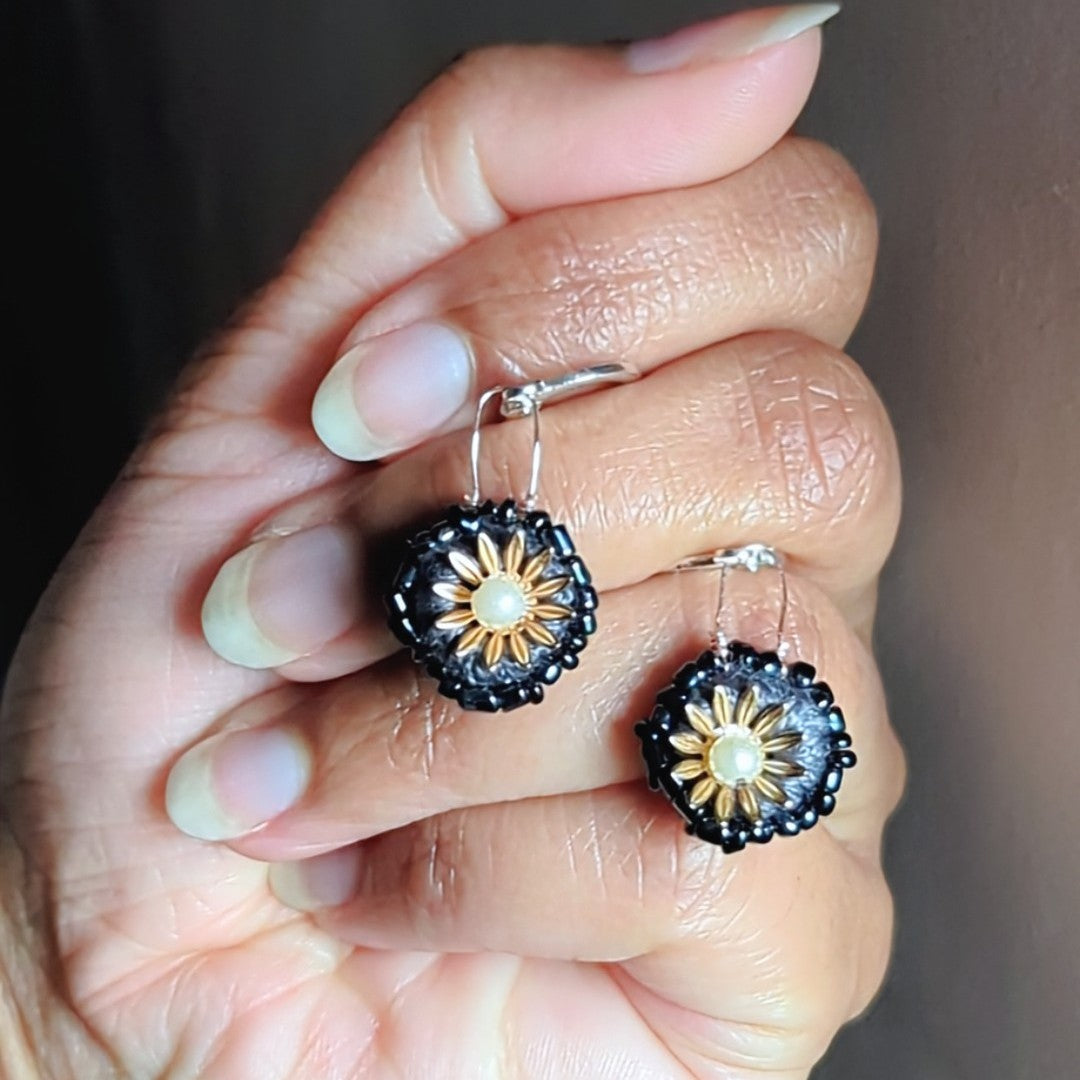 Hand holding a grey gold beaded floral motif pair of Indian designer earrings made for Mayaani Jewellery UK.