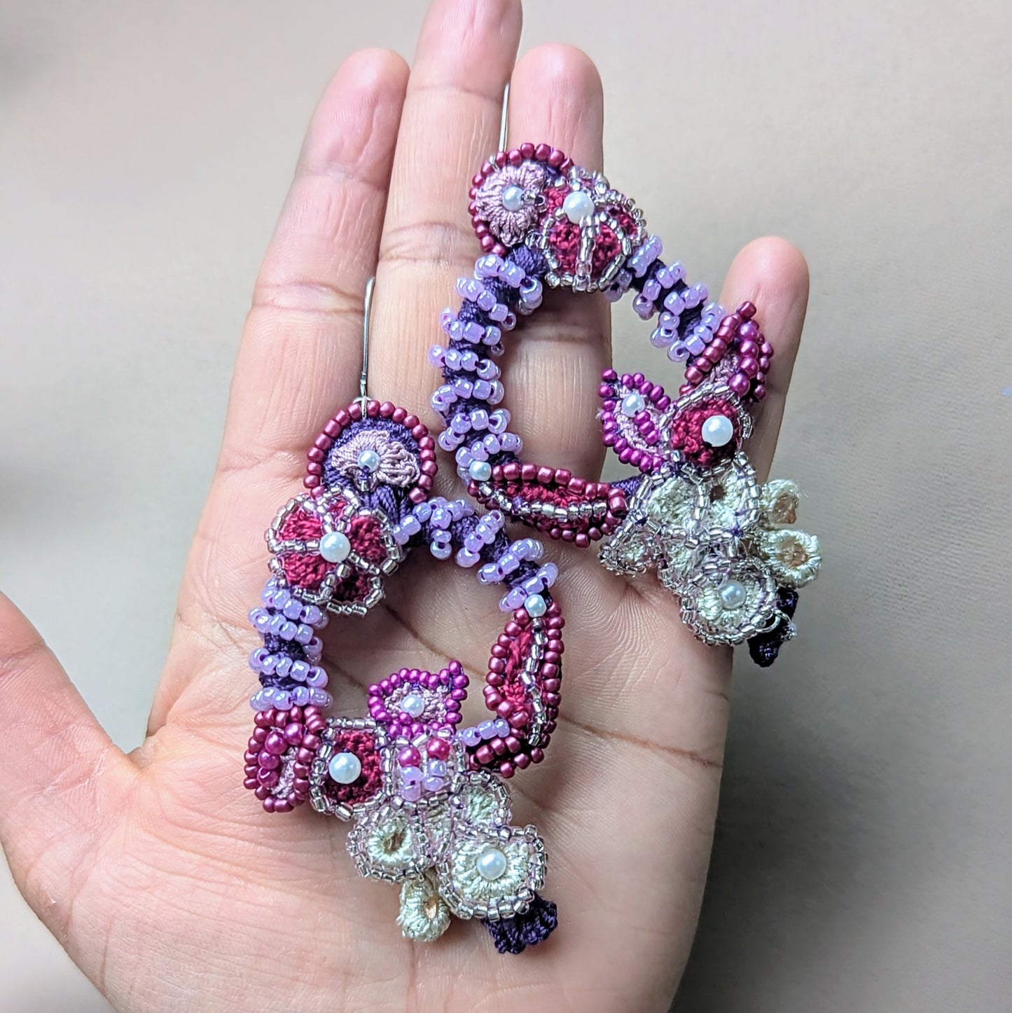 Close-up of Mayaani Jewellery's 'Gulab Rani' bridal earrings, handcrafted with glass seed beads in shades of red, purple, and ivory. The floral-inspired design features intricate bead embroidery and crochet, with layered textures and cascading beadwork for statement bridal look.