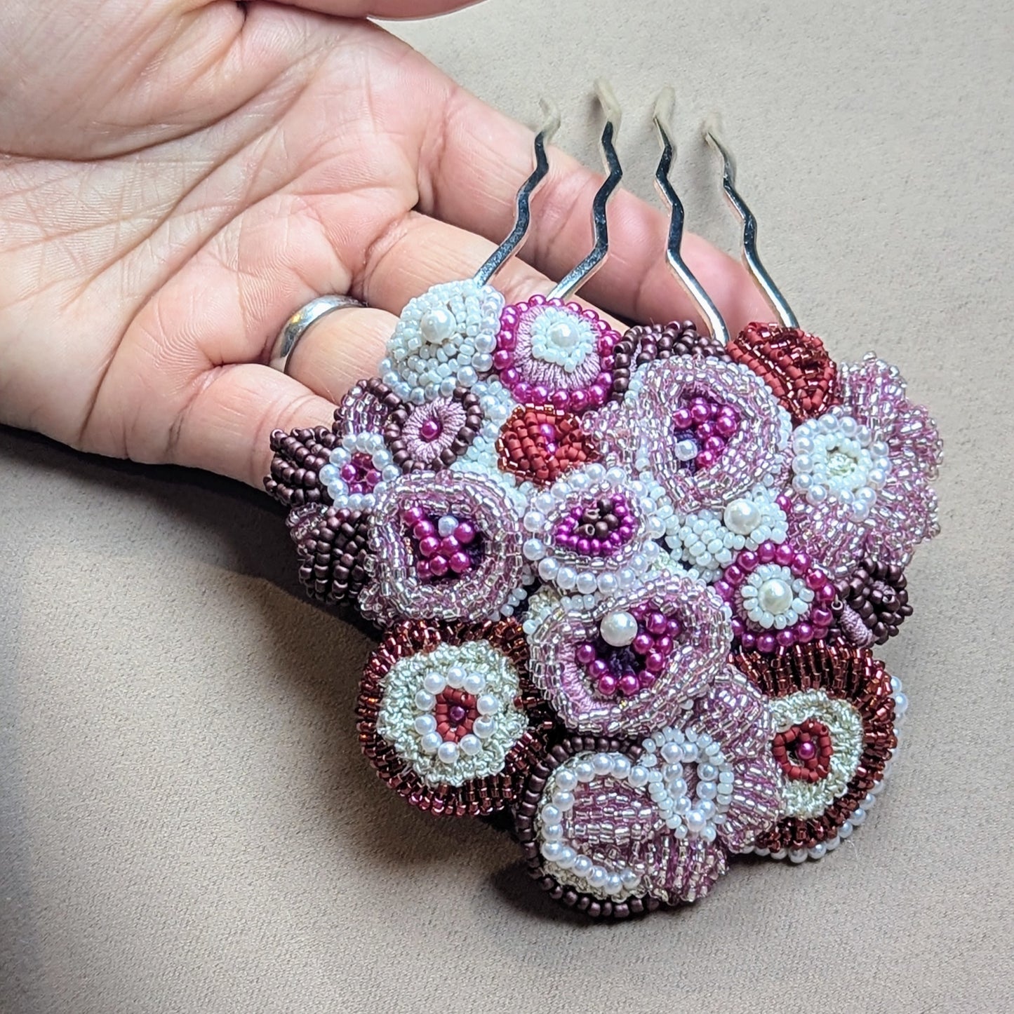 Handcrafted Indian bridal hair pin from the 'Gulab Rani' jewellery set by Mayaani Jewellery, featuring stainless steel prongs intricately hand-beaded floral motifs. Designed with concentric circles and adorned with pearl seed beads in shades of red, pink, purple and ivory.