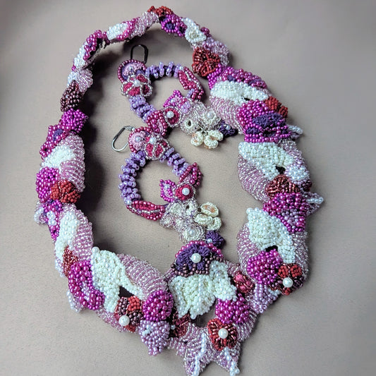 A one-of-a-kind handcrafted Indian bridal jewellery set named 'Gulab Rani' by Mayaani Jewellery, featuring bead embroidery, hand crochet, and wirework in elegant shades of purple, red, pink and pearl white on a neutral background. The image shows a necklace with detachable pendant and pair of earrings ethically made in the UK with glass seed beads designed for modern brides who honour tradition.