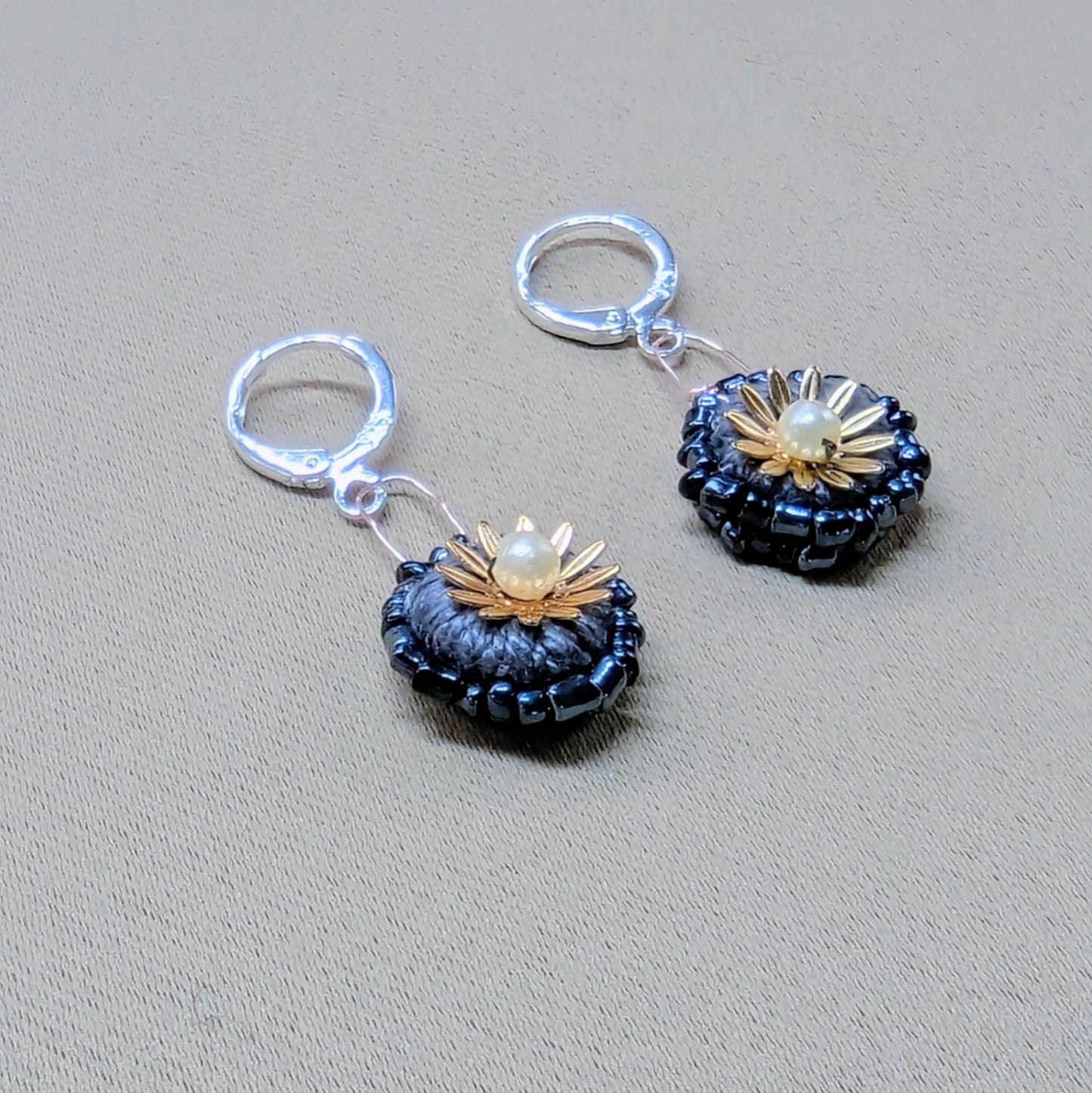 Flat lay side view of handmade grey and gold floral earrings featuring vintage seed pearls and glass seed beads.