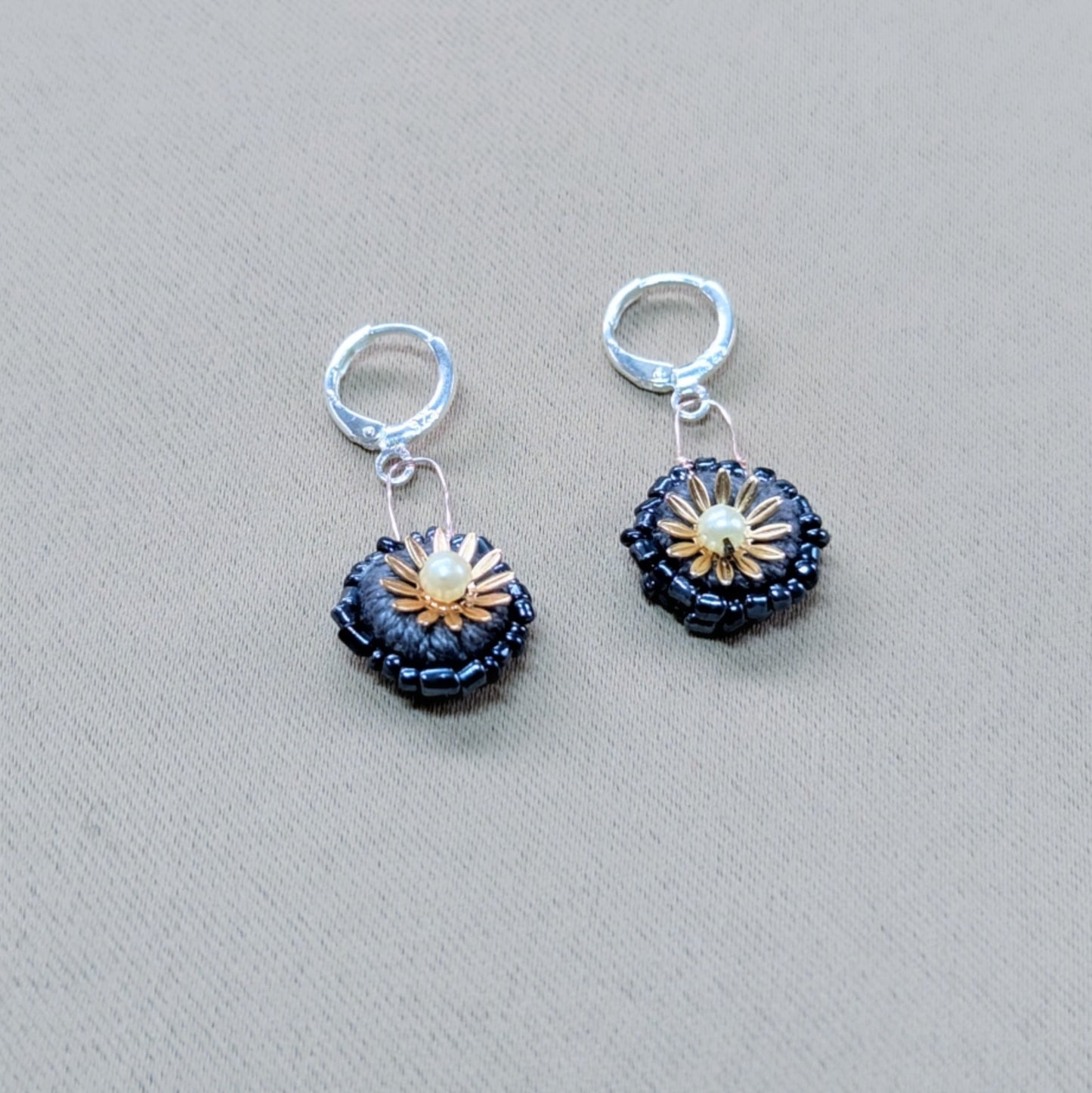 Close-up of a small pair of earrings - featuring hand crochet, bead and wire artistry on a soft grey fabric backdrop.