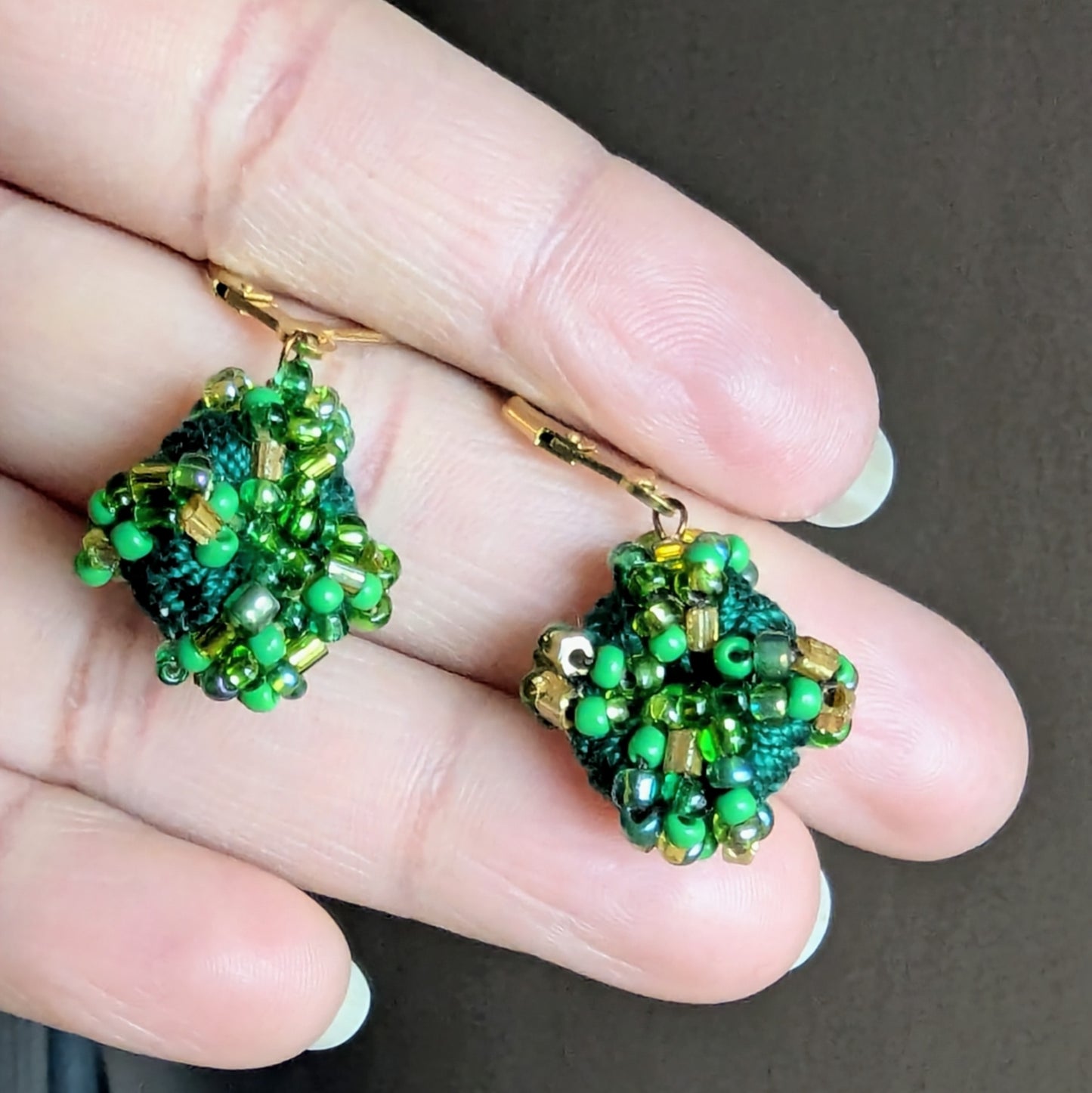 A close up view of a hand holding an intricately woven everyday pair of Indian heritage inspired bead earrings.