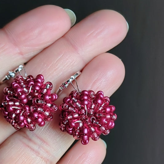 Hand holding one-of-a-kind berry pink handmade earrings crafted with silver-lined seed beads and rose gold copper wire by Mayaani Jewellery UK.