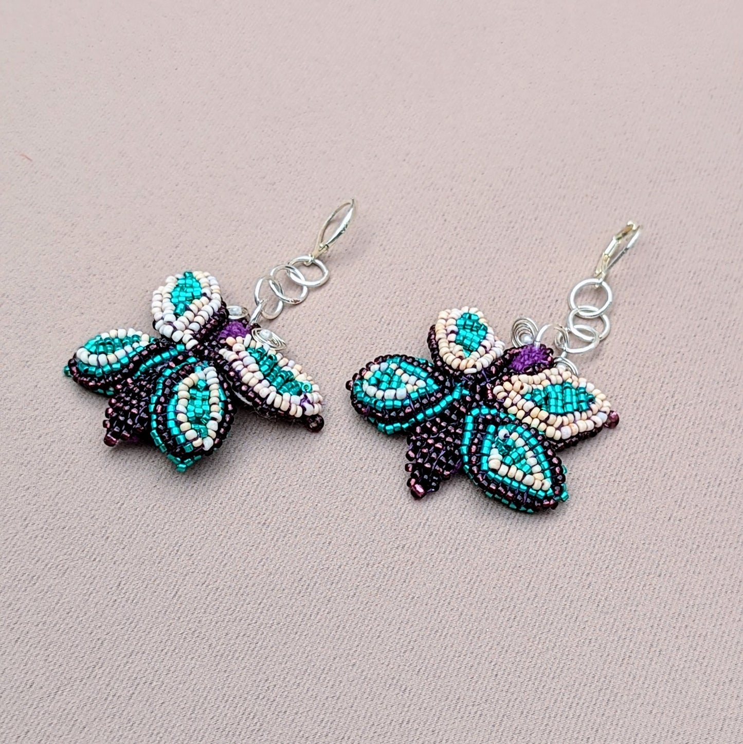 A close up view of a one-of-a-kind pair of purple, blue, silver and cream butterfly shaped earrings exclusive to UK brand Mayaani Jewellery.