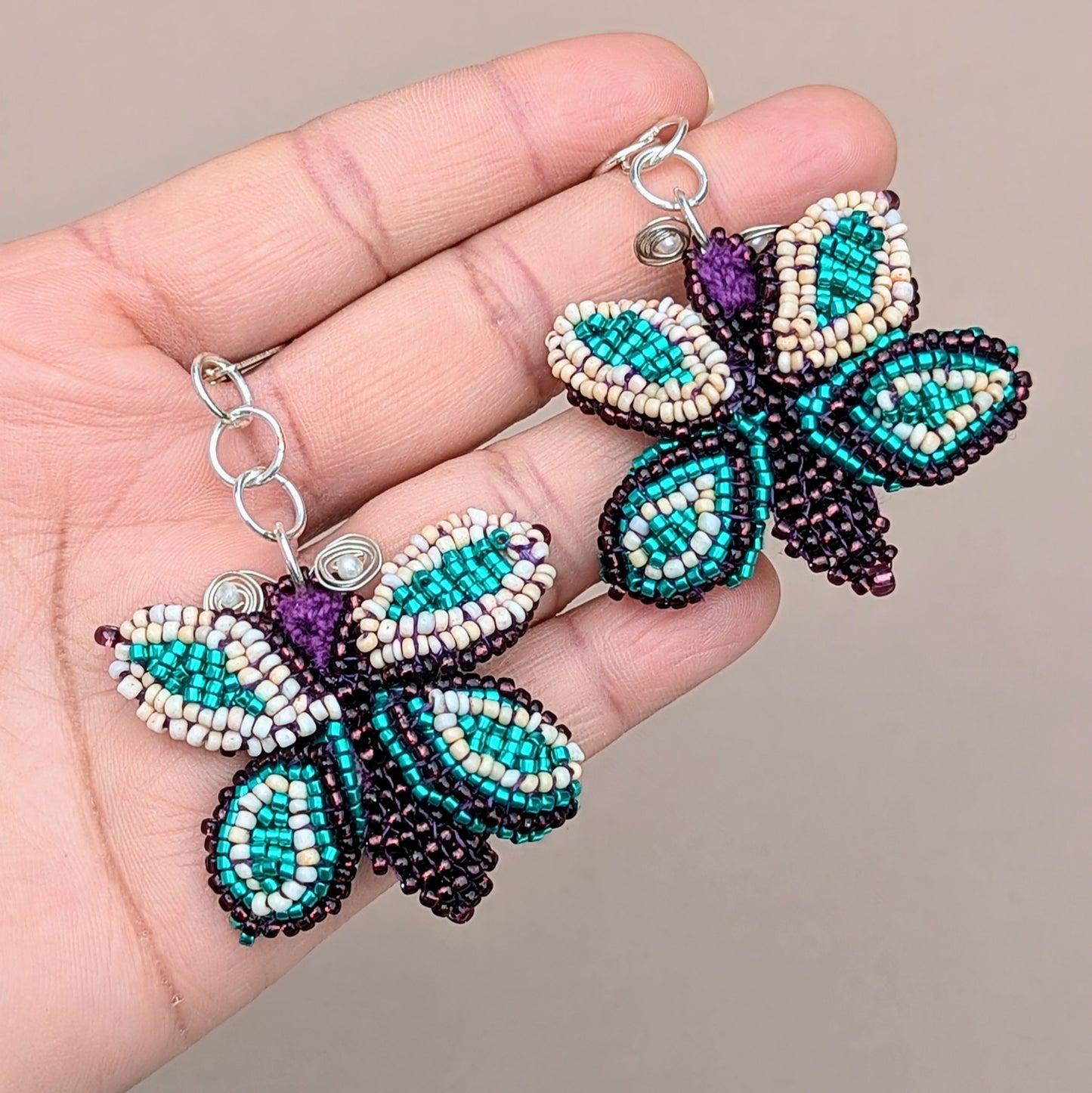 Hand holding a pair of vibrant blue, purple, cream and silver butterfly earrings designed and handmade for Mayaani Jewellery UK using sustainable practices.