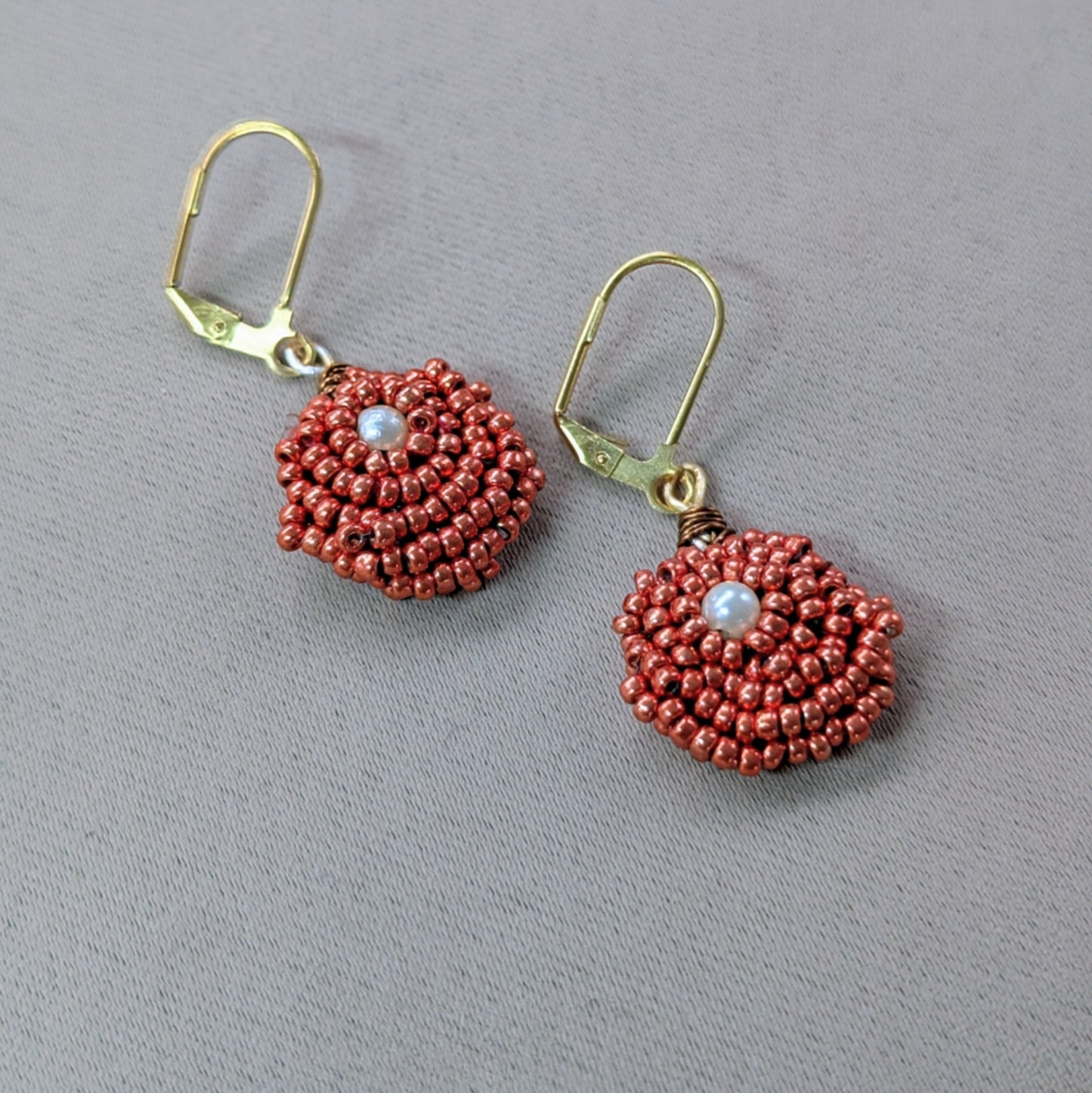 Close up of an artisan handmade pair of copper and pearl seed bead earrings.