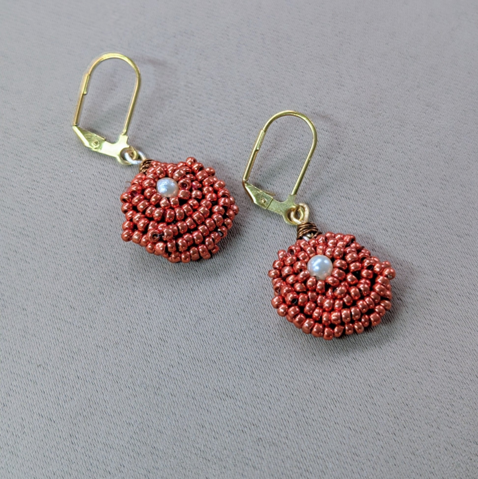 Close up of an artisan handmade pair of copper and pearl seed bead earrings.