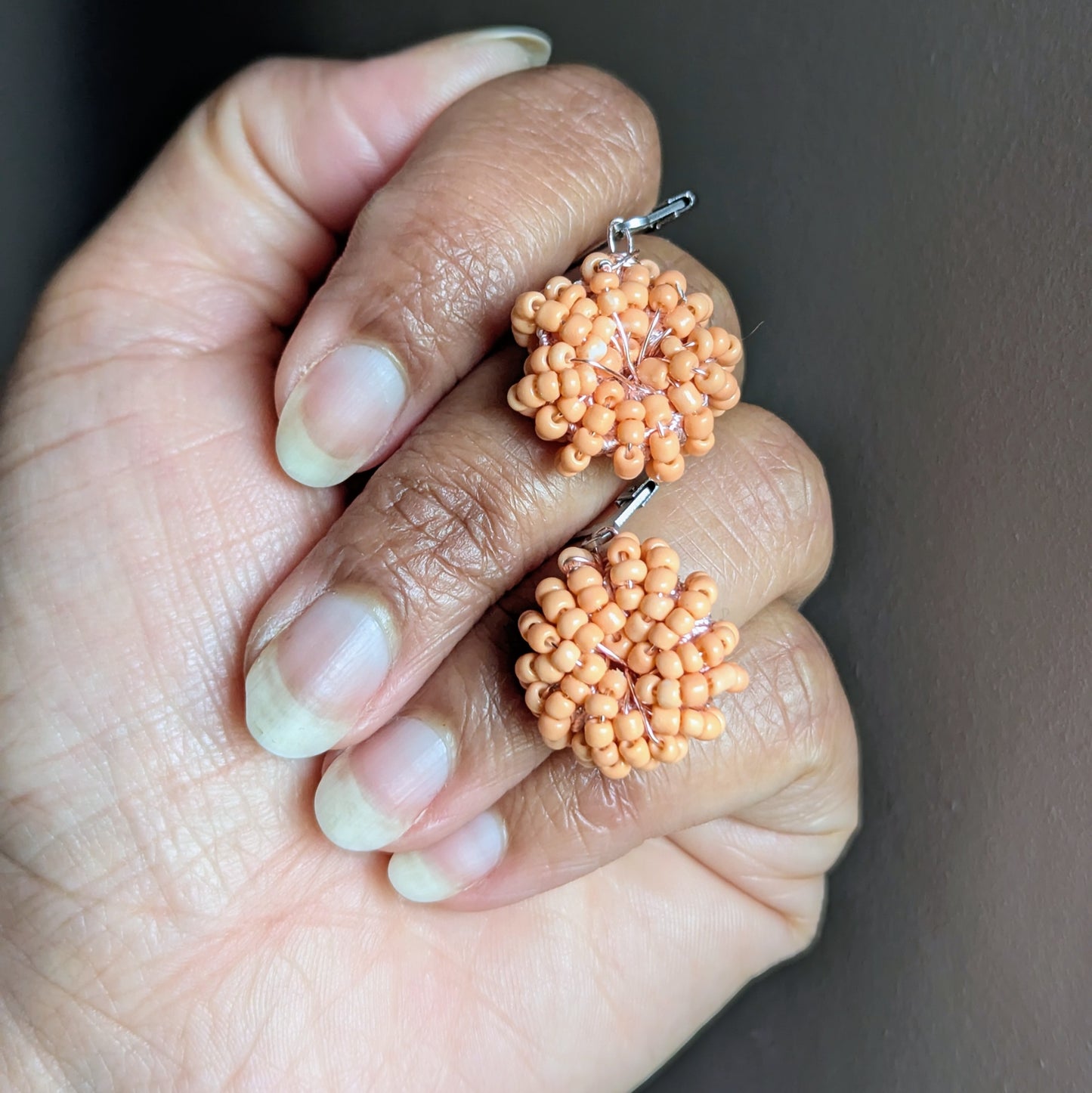 Close-up of delicate peach beaded earrings on neutral background.
