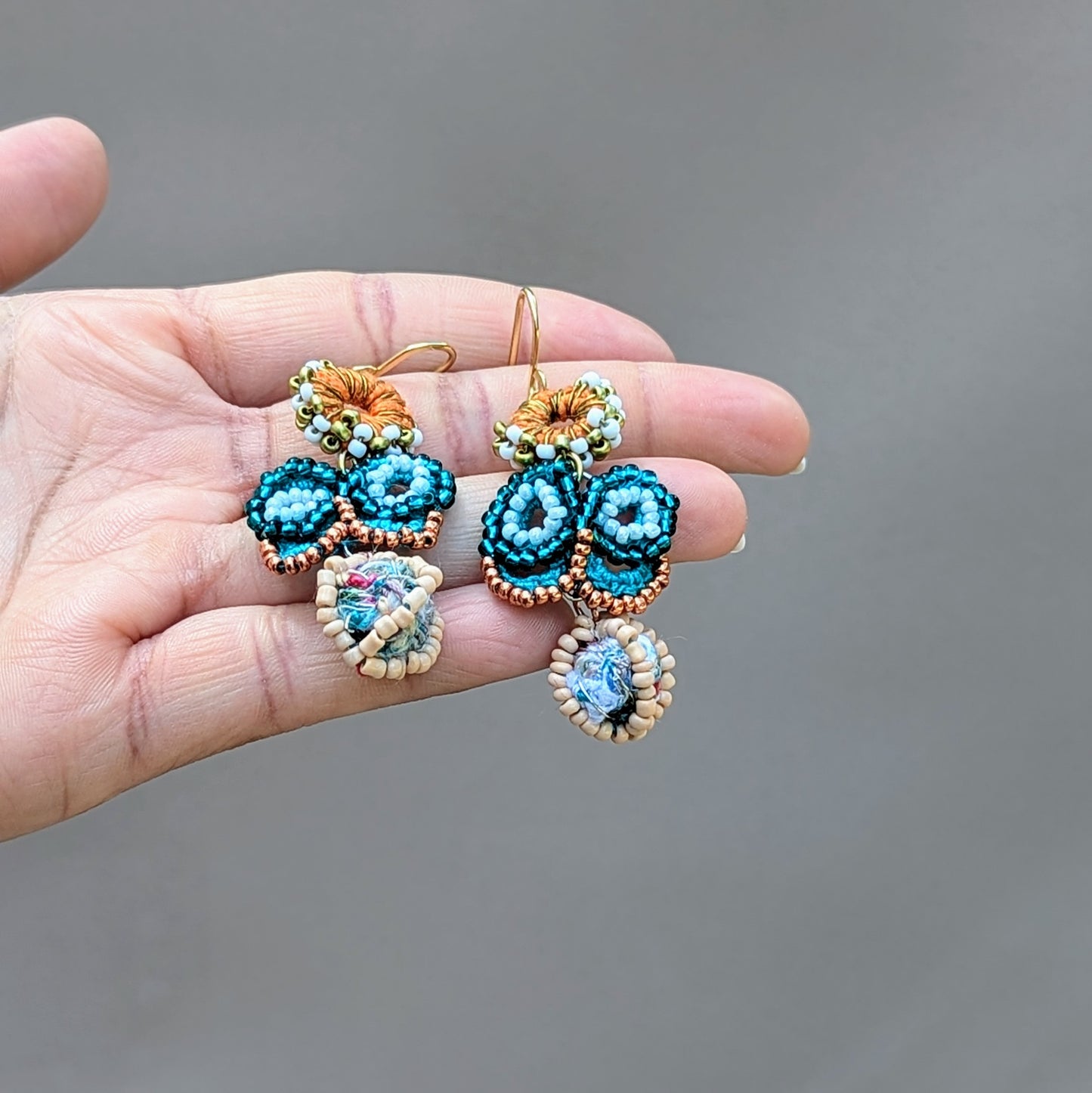 Hand holding a one-of-a-kind blue butterfly earrings with seed bead and crochet detailing, perfect for weddings or special occasions. Ethically handcrafted using vintage upcycled materials by Mayaani Jewellery UK.