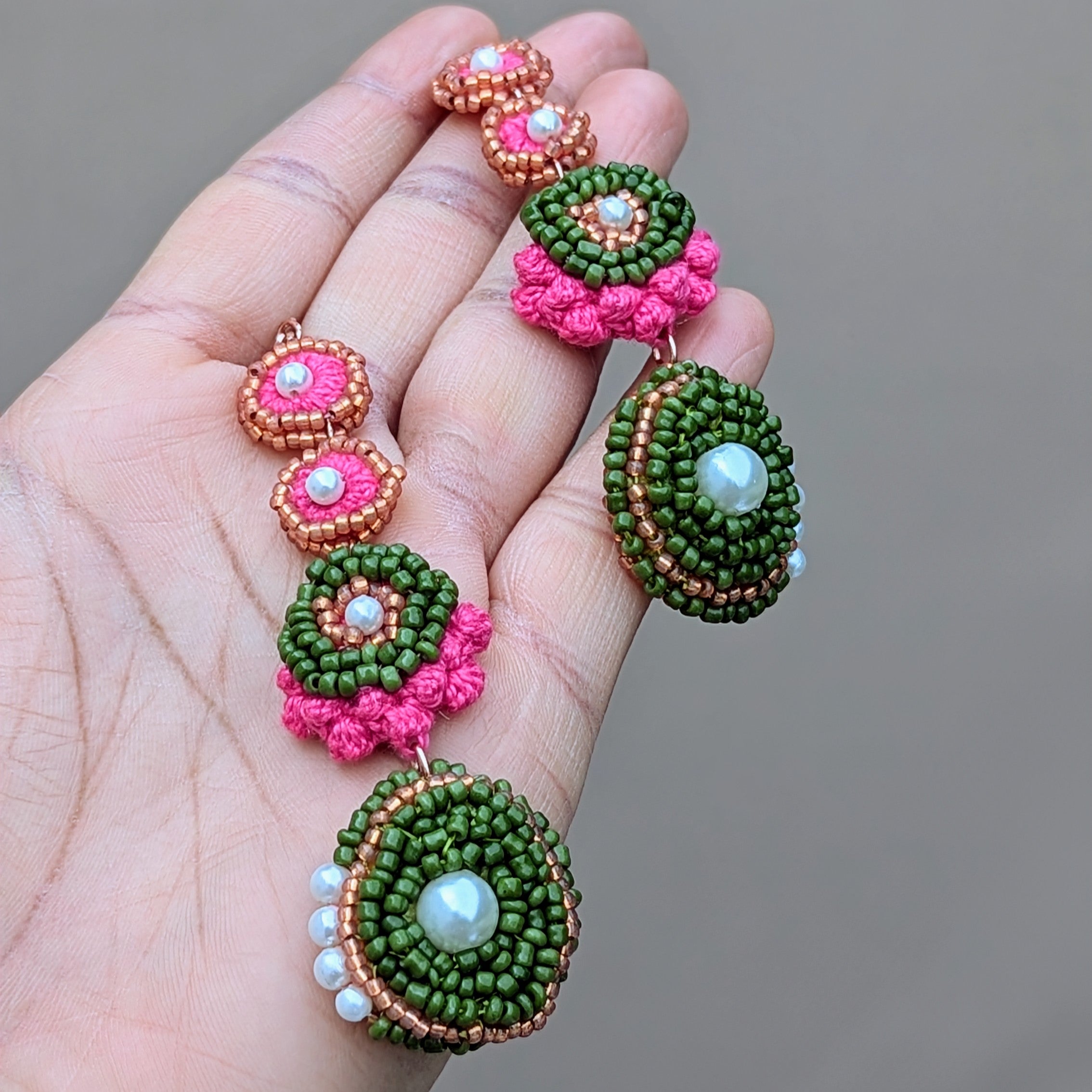Hand holding a pair of pink, green, seed pearl Indian style crochet bead earrings sustainably handcrafted in the UK at Mayaani Jewellery.