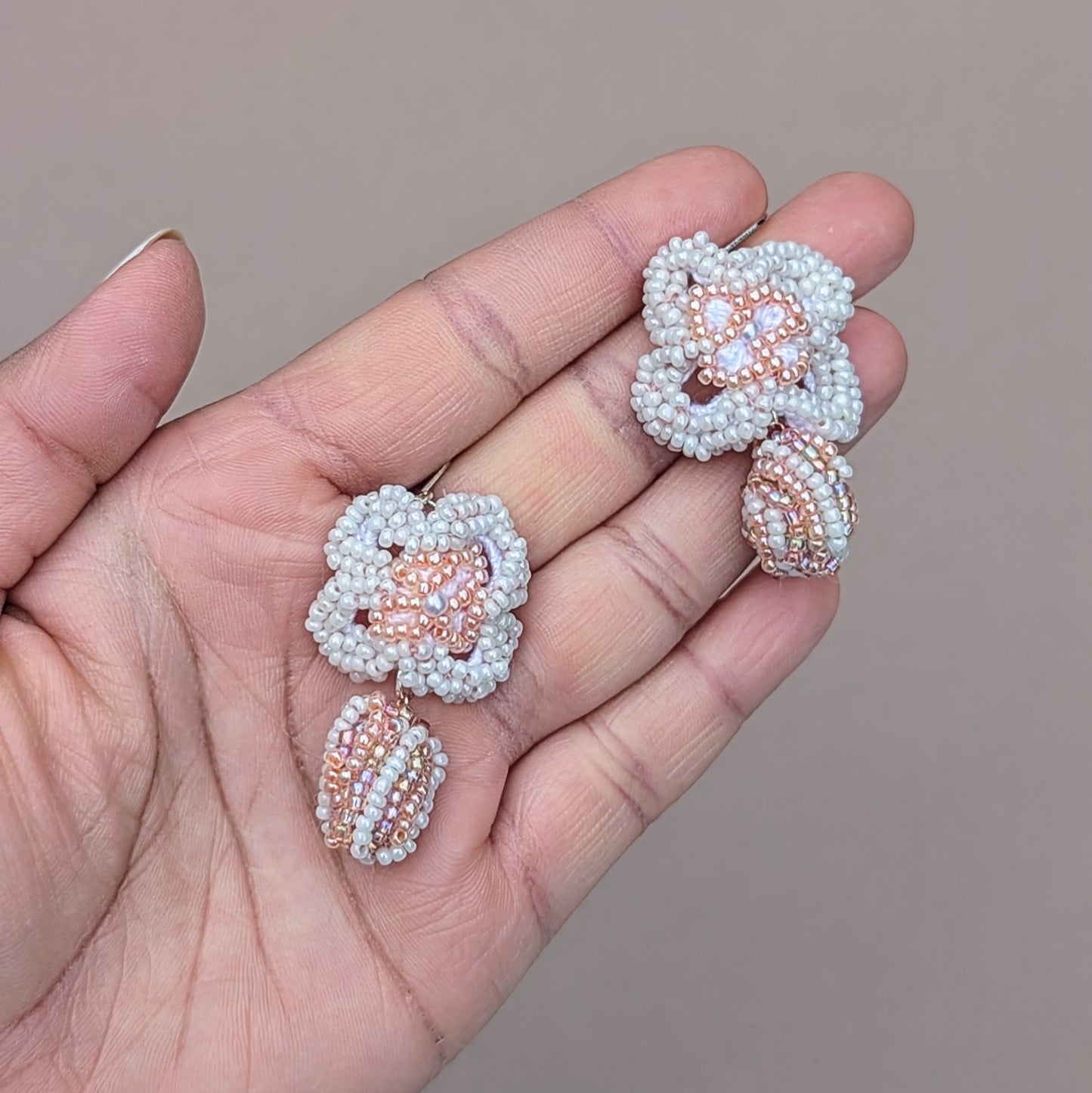 Eco-friendly earrings in a soft bridal palette of peach and white, displayed against a neutral linen backdrop. The design features seed bead florals, upcycled scrap beads, and 25 silver lever-back hooks.