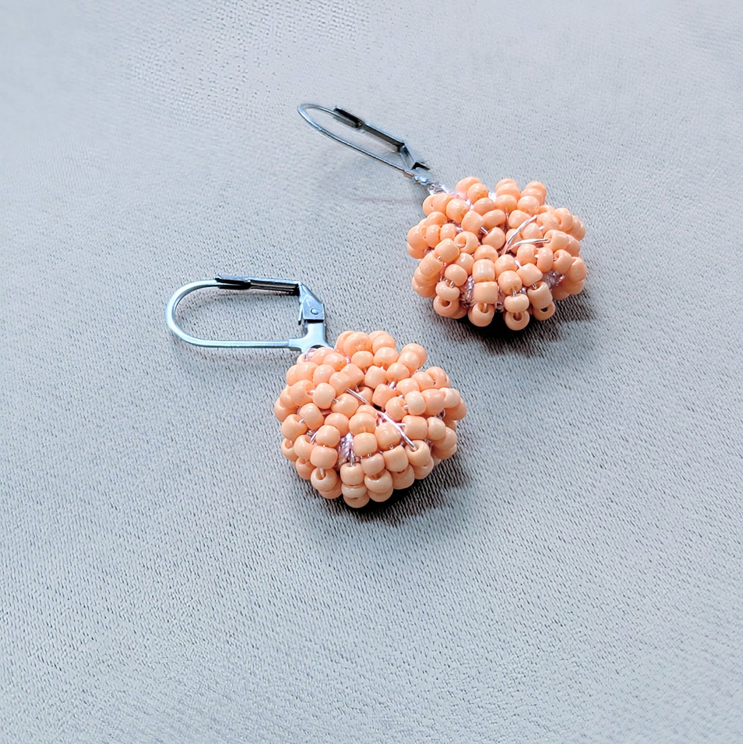 Hand holding luxury peach bead earrings handcrafted in the UK.