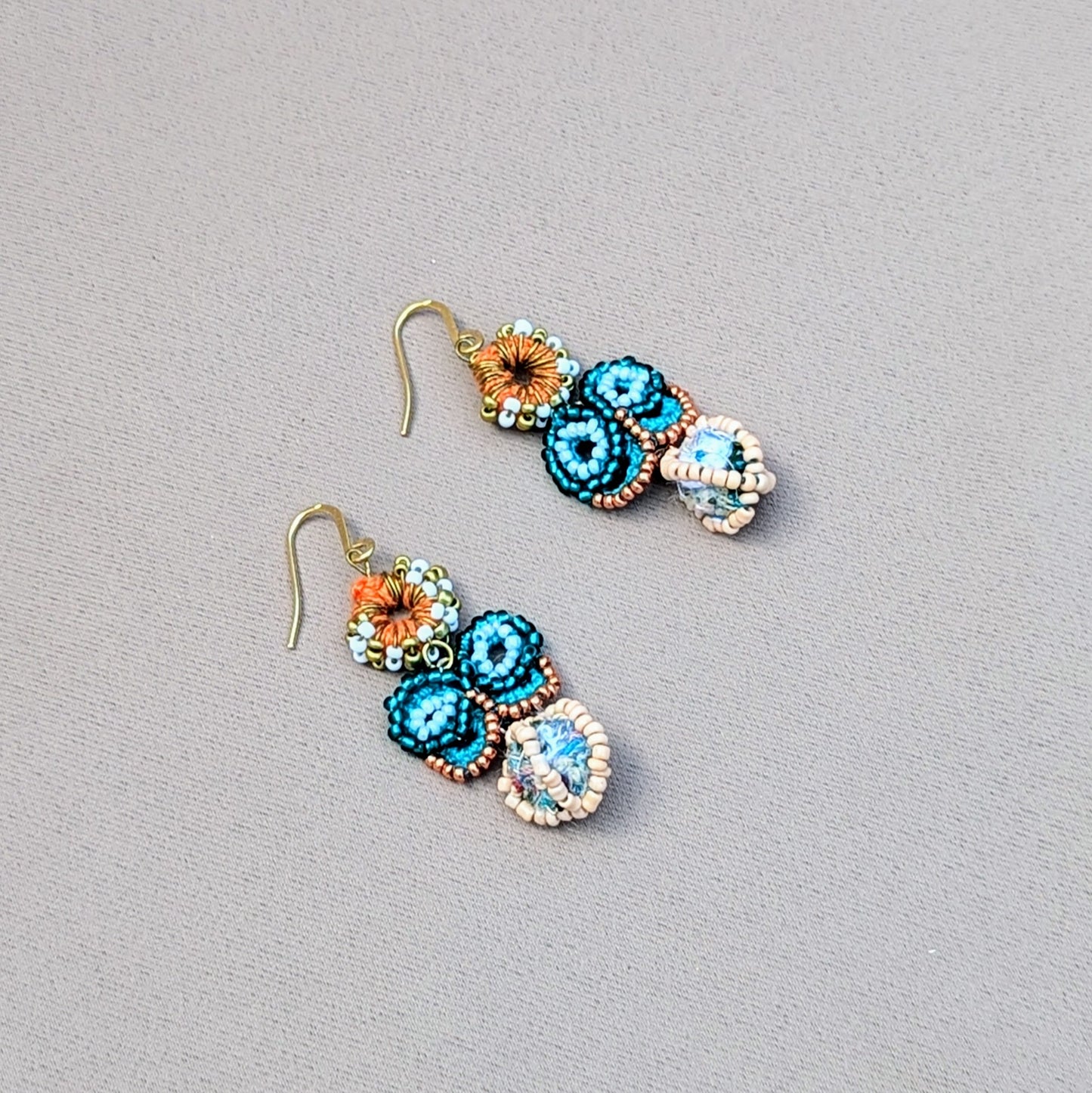Turquoise and rose gold beaded butterfly earrings on a neutral backdrop, with orange crochet, white, and gold seed beads, and a handmade scrap bead. Sustainable, Indian-inspired statement earrings by Mayaani Jewellery UK.