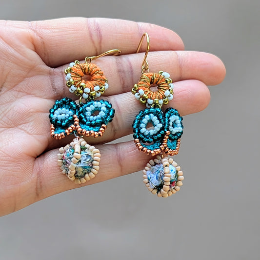 Handmade Indian butterfly earrings held in a hand, featuring turquoise, rose gold, and orange with sustainable scrap beads. Designed by eco-conscious brand Mayaani Jewellery UK.