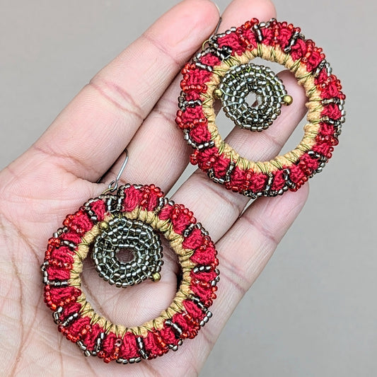 Hand holding a pair of red hot sun one-of-a-kind beaded earrings handcrafted with upcycled beads.