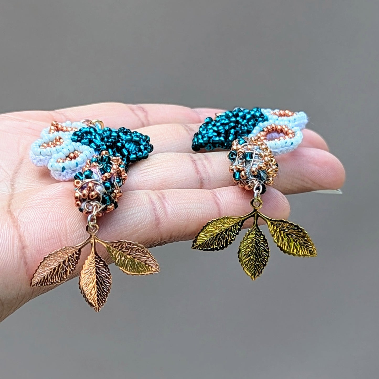 An asymmetric pair of seahorse inspired earrings featuring emerald green, rose, gold and white seed beads paired with signature Mayaani Jewellery scrap beads and gold and rose gold plated leaf charms.