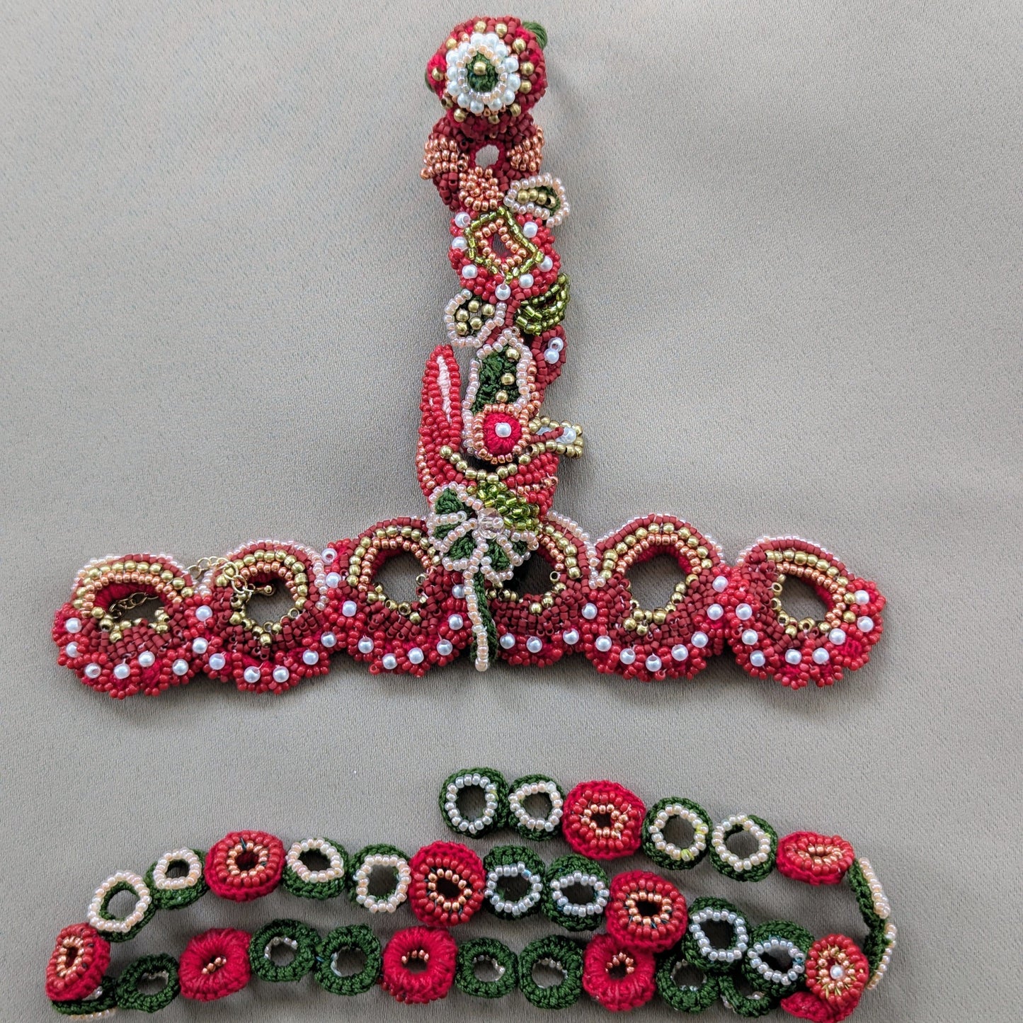 Flat lay image of the Shreya 5-in-1 red green gold bead crochet Indian hand harness bracelet with custom bead crochet chain on a neutral grey backdrop.
