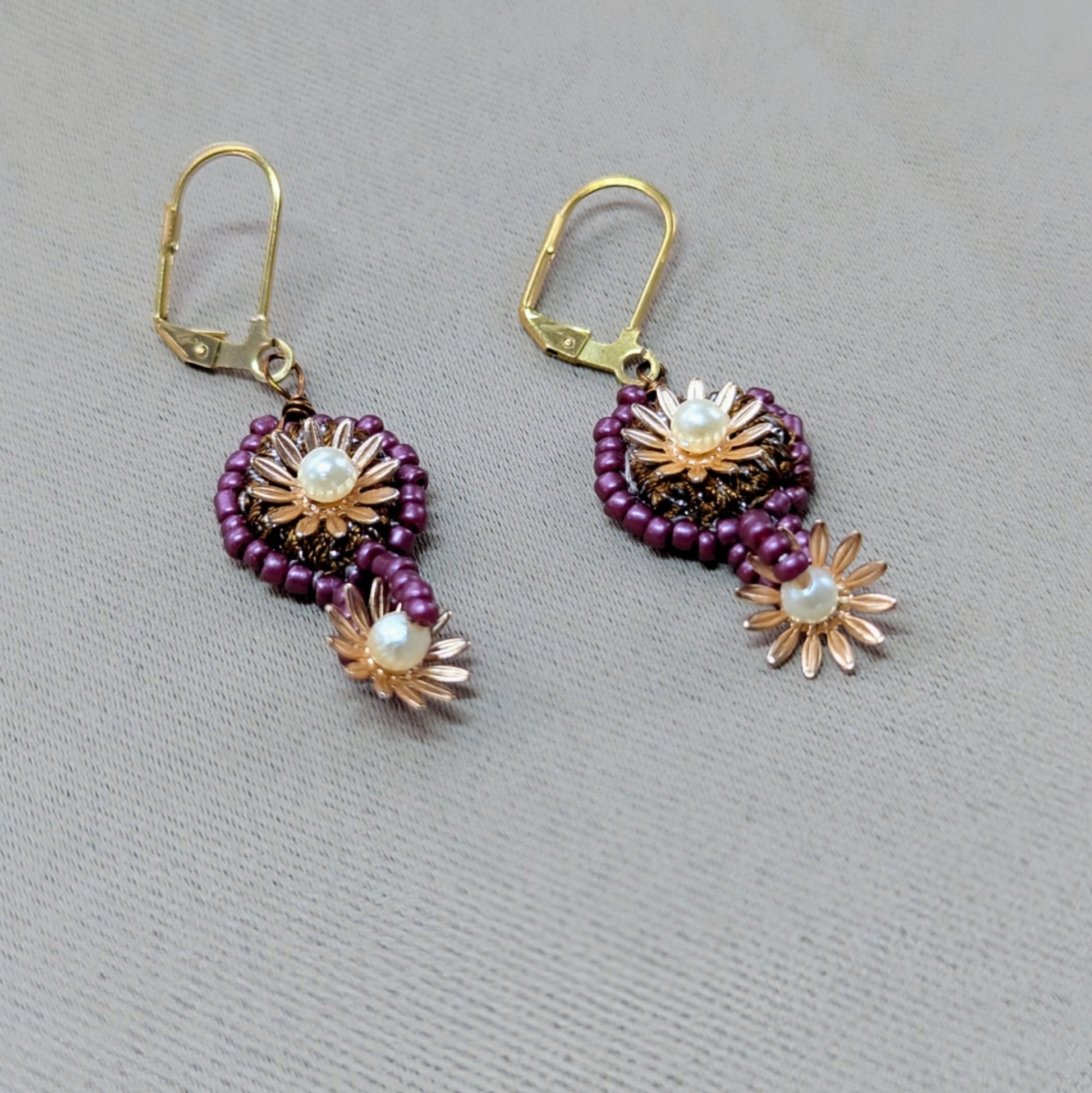 Close-up of Indian-inspired artisan earrings in purple and gold tones featuring seed pearl accents and intricate crochet beadwork.