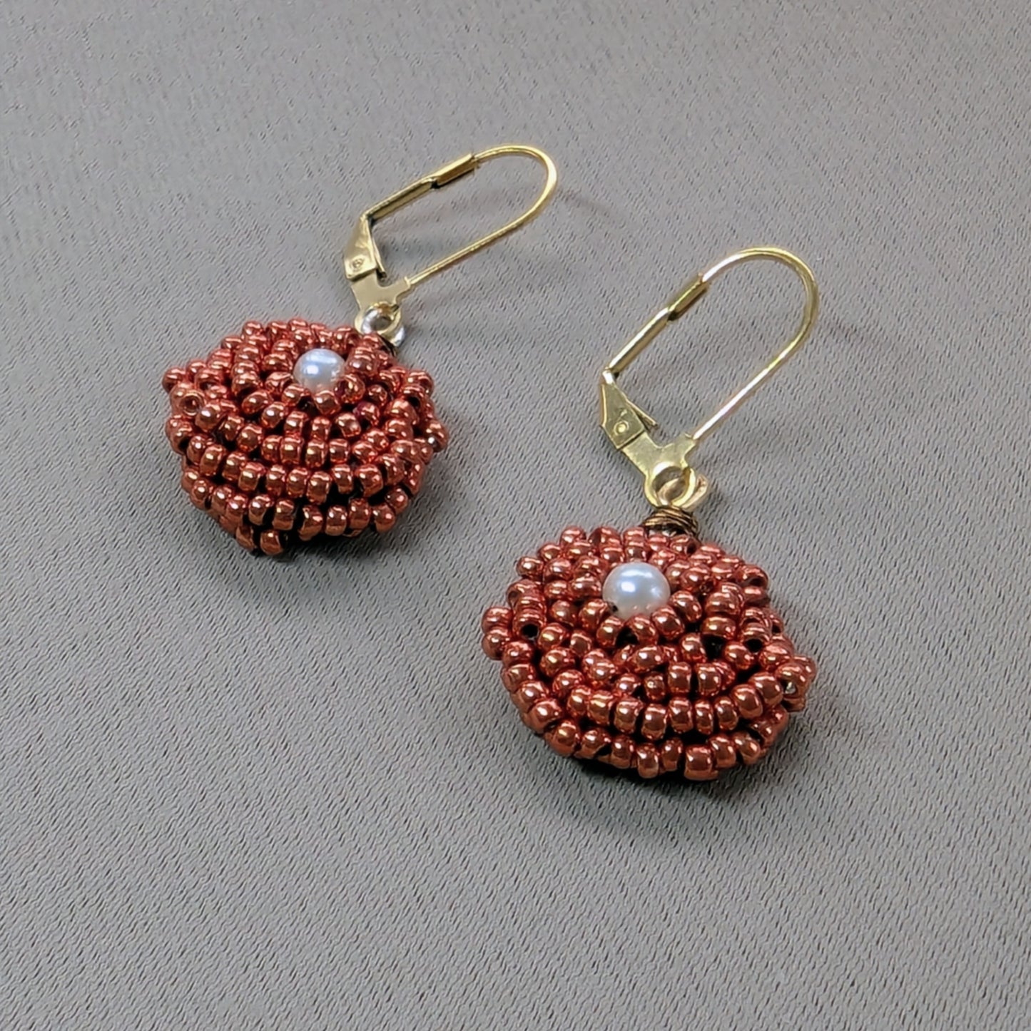 Close up view of a one-of-a-kind pair of artisan handcrafted copper and vintage pearl seed bead earrings.