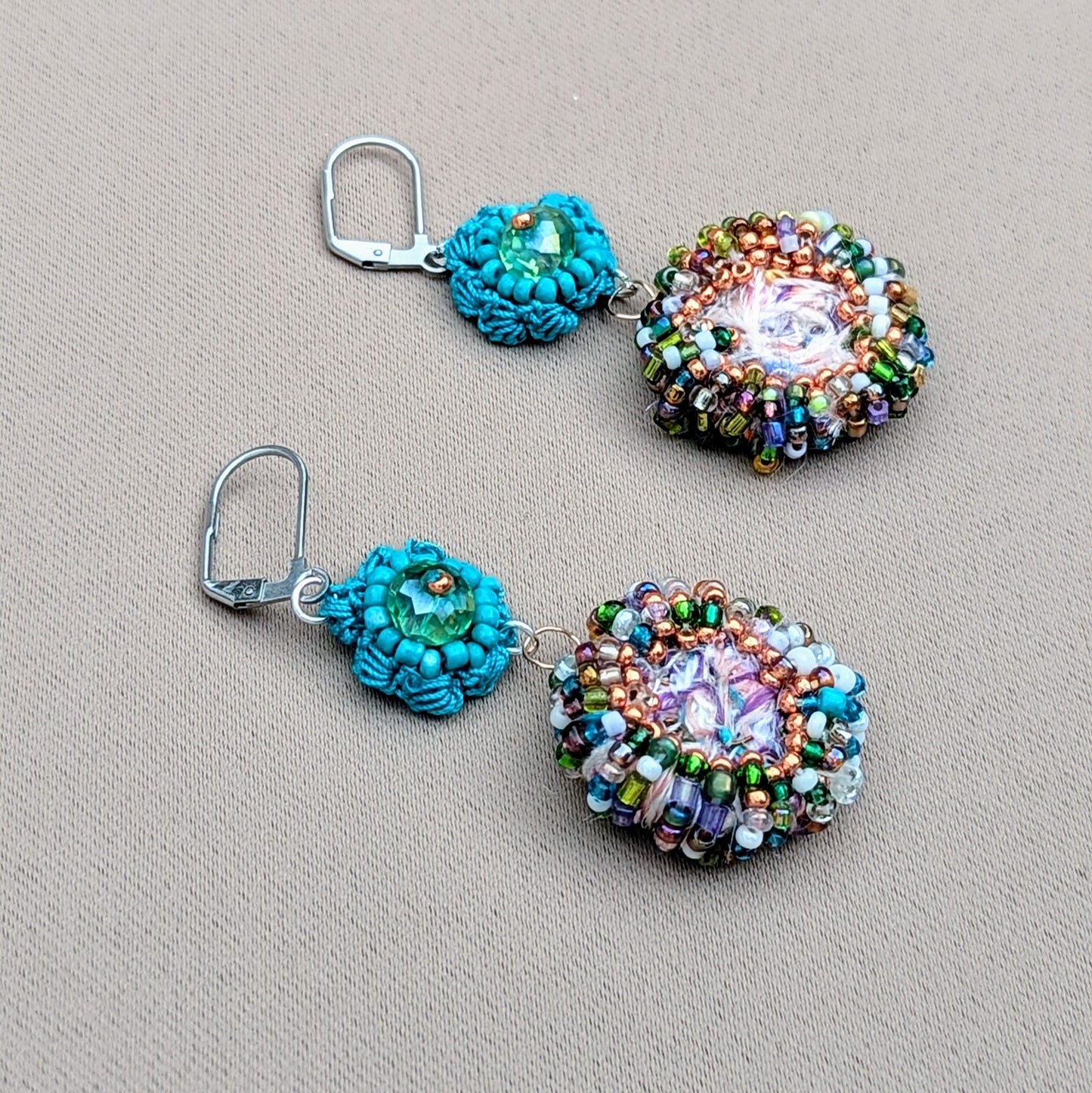Close-up of a hand holding vibrant handcrafted earrings made with Mayaani Jewellery's signature scrap bead technique. Colours include turquoise, rose gold, purple, green, and light blue.
