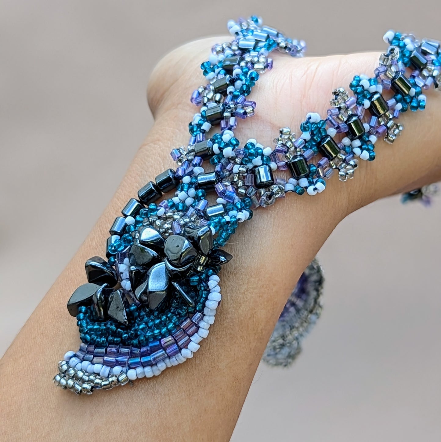 Close-up of a person's wrist displaying a colourful blue, lilac, hematite beaded necklace expertly handcrafted for Mayaani Jewellery UK.